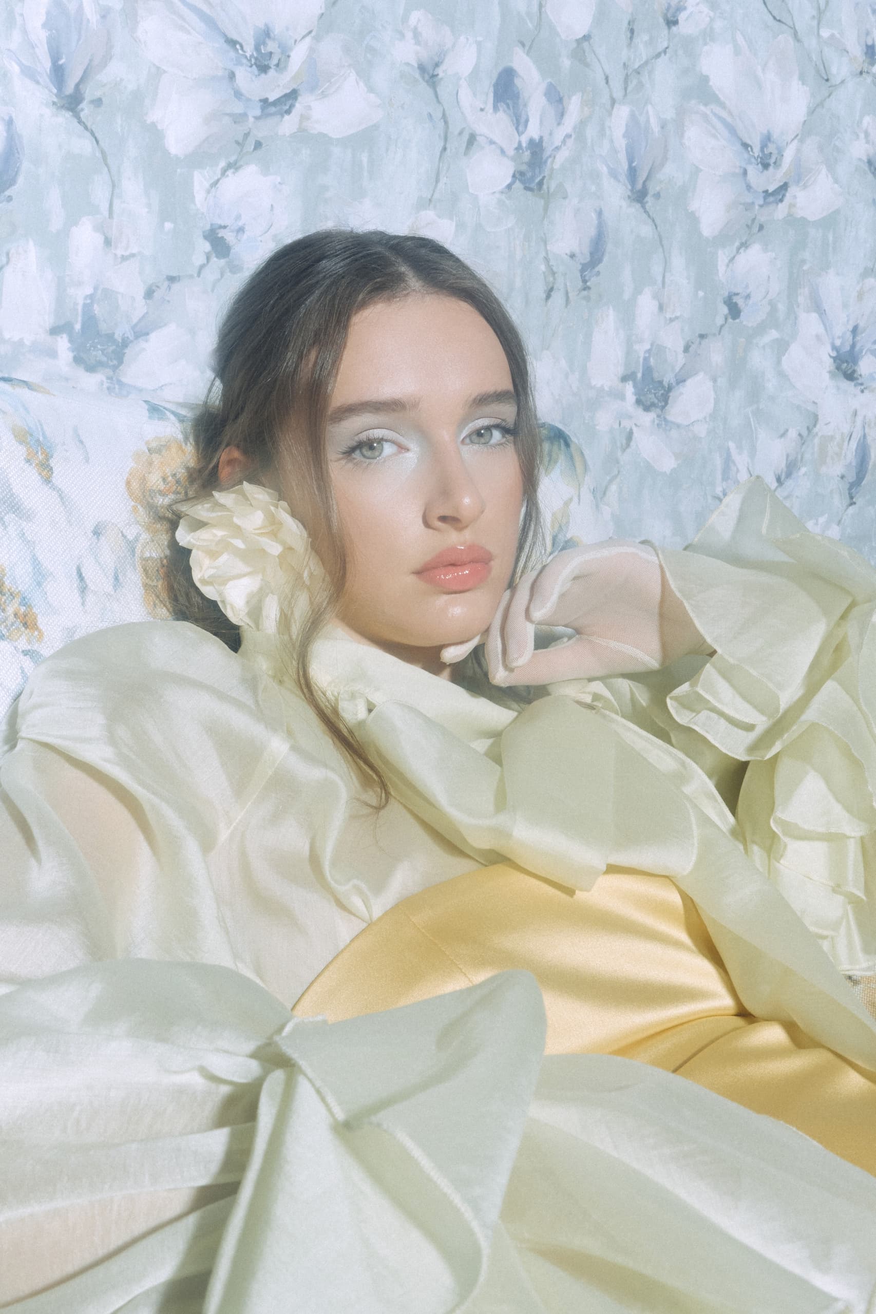 Elegant woman in pastel fashion with floral backdrop, serene and stylish.