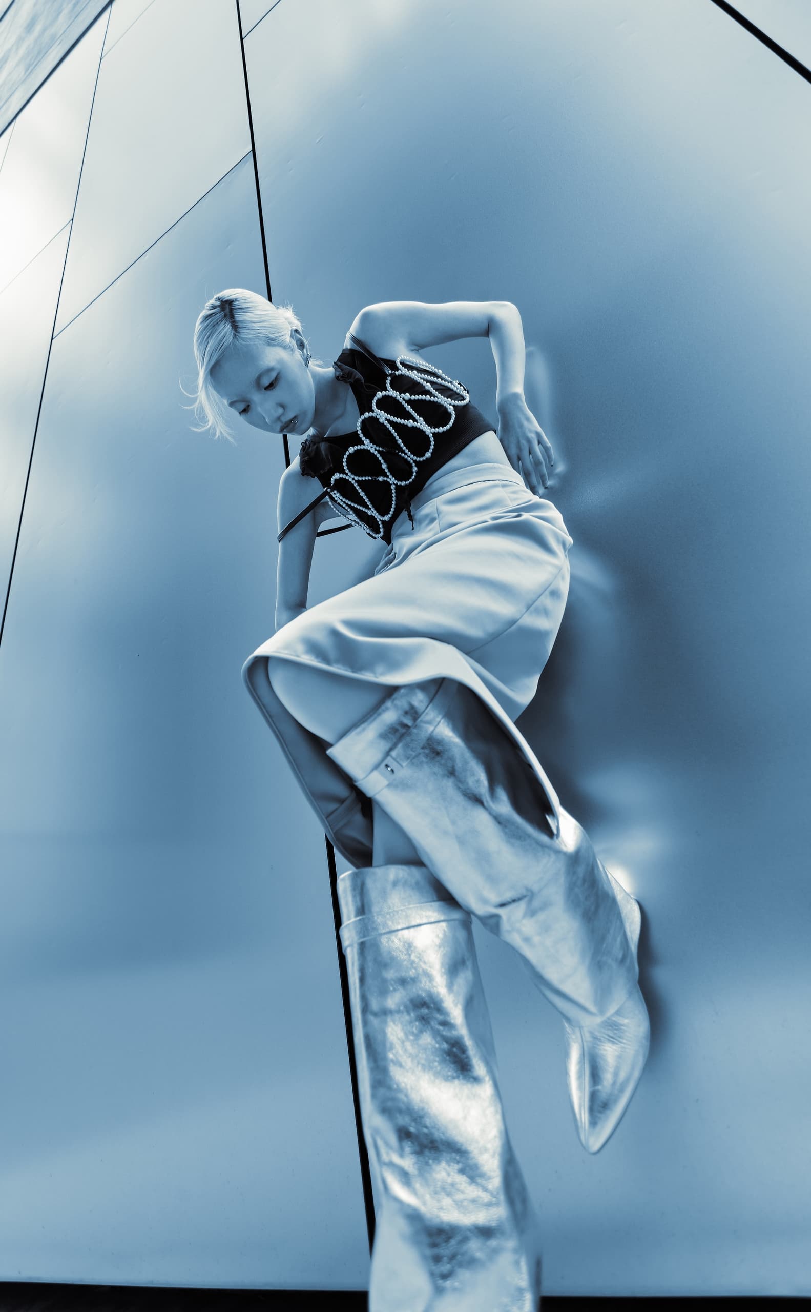 Futuristic fashion: model in bold silver boots and edgy top against modern backdrop.