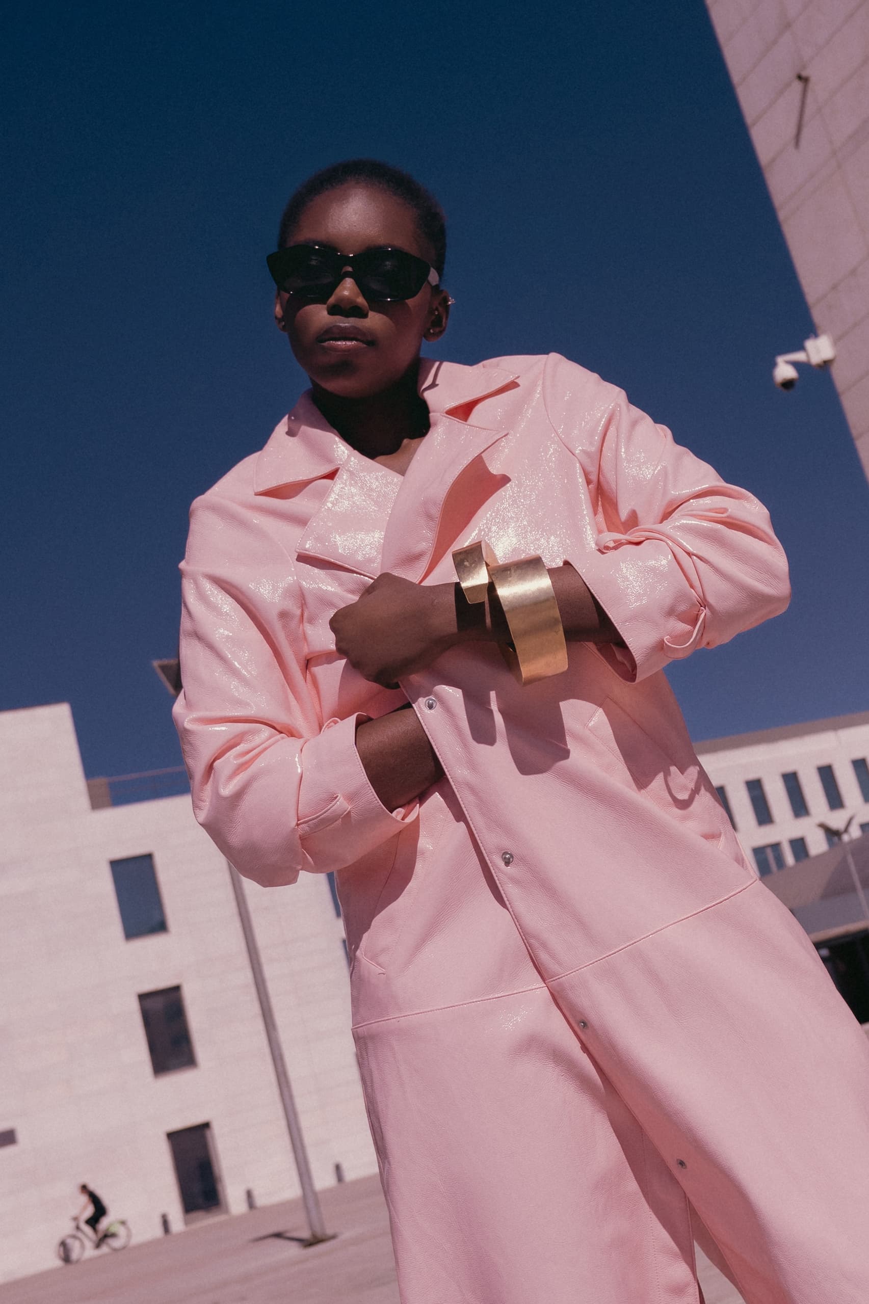 Fashionable person in pink coat with gold bracelet under clear blue sky.