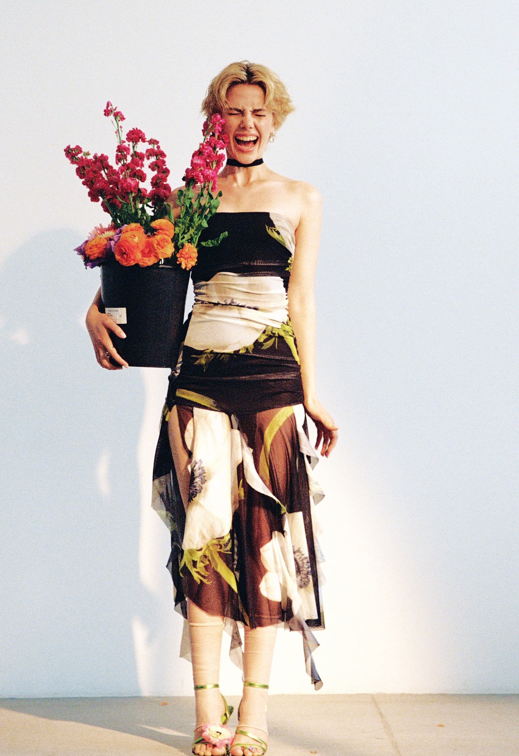 Woman in floral dress holding a vibrant flower bouquet, smiling with joy.
