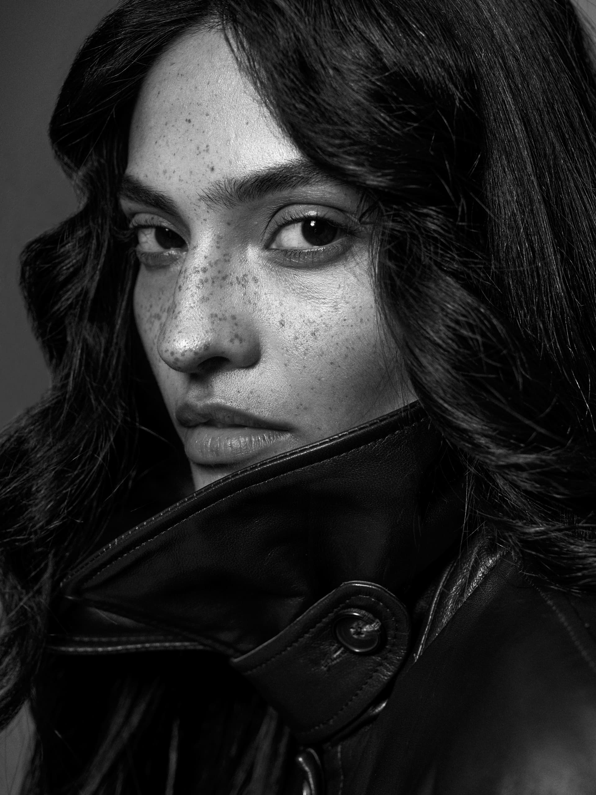 Close-up of woman with freckles wearing a leather jacket, in black and white.
