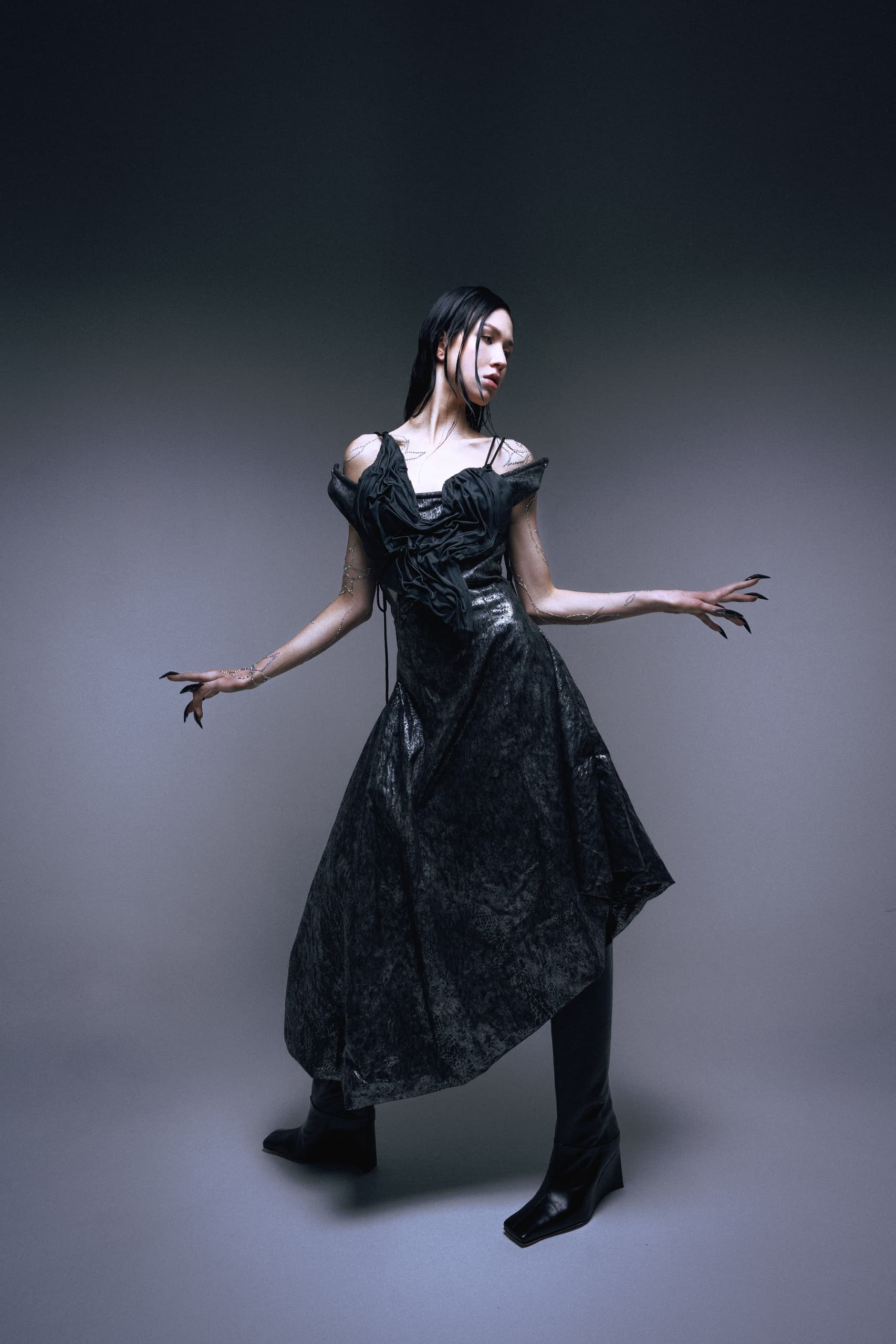 Elegant person in gothic black dress posing with long nails and boots.