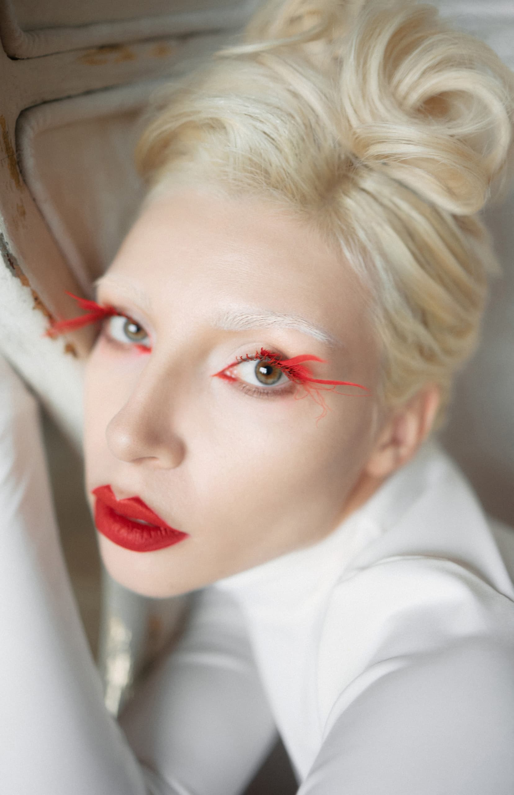 Woman with bold red makeup and white hair, striking avant-garde fashion look.