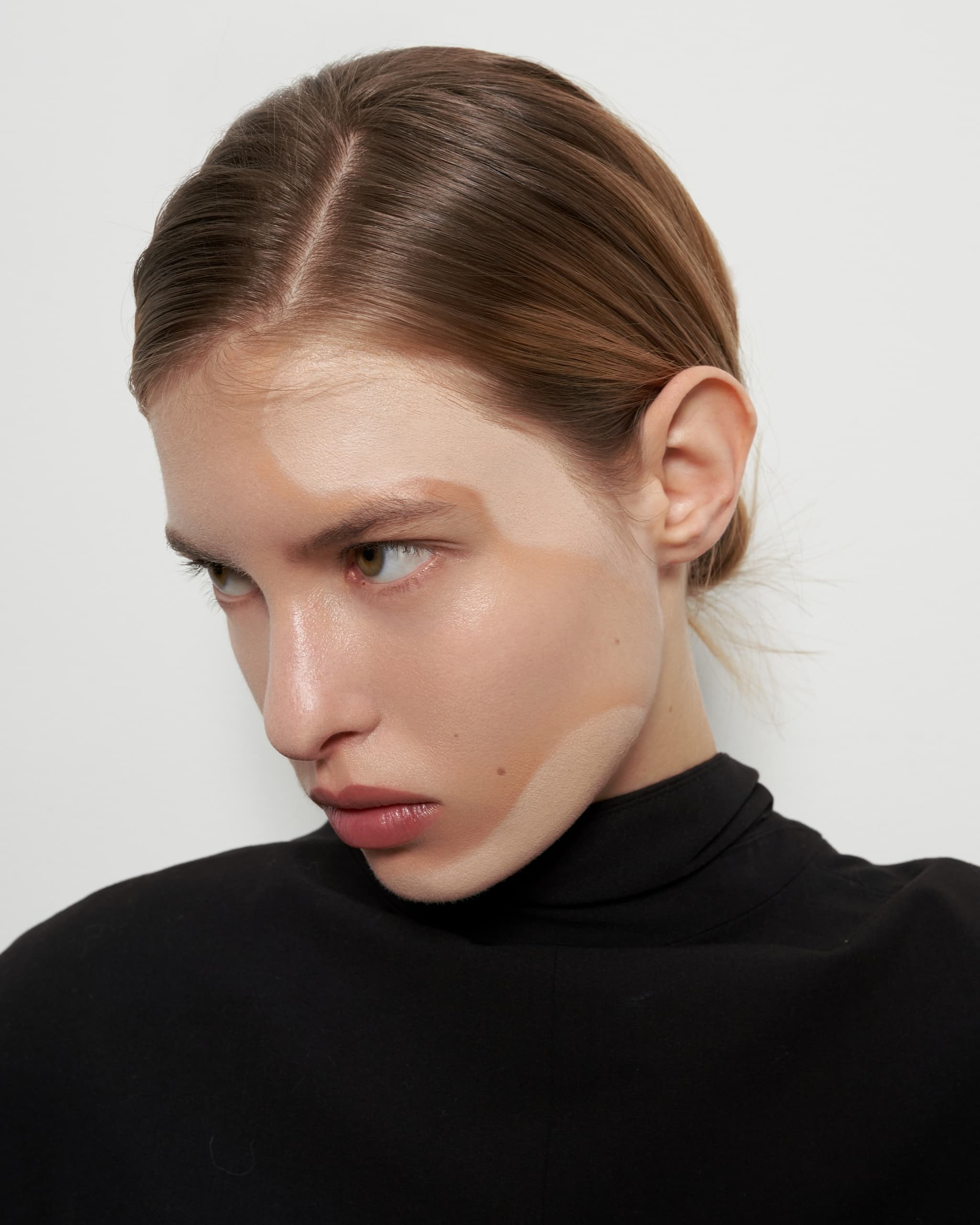 Close-up of a person with sleek hair and defined facial contouring in a black top.