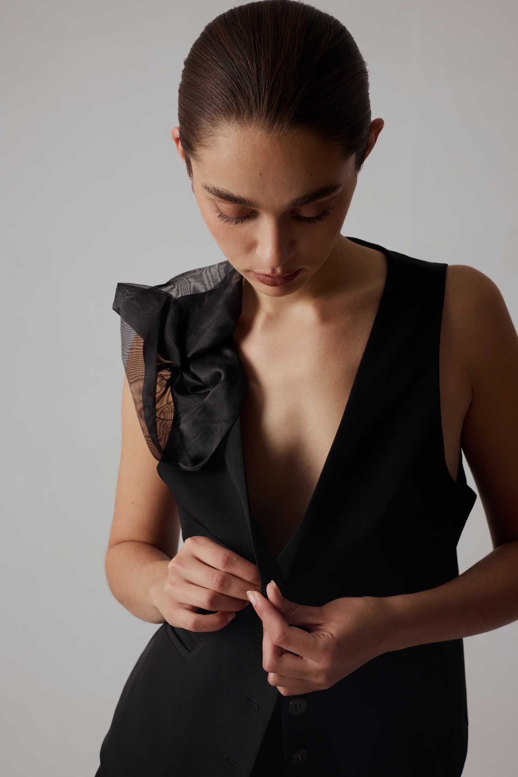 Woman in stylish black outfit adjusts button, showcasing elegant fashion design.