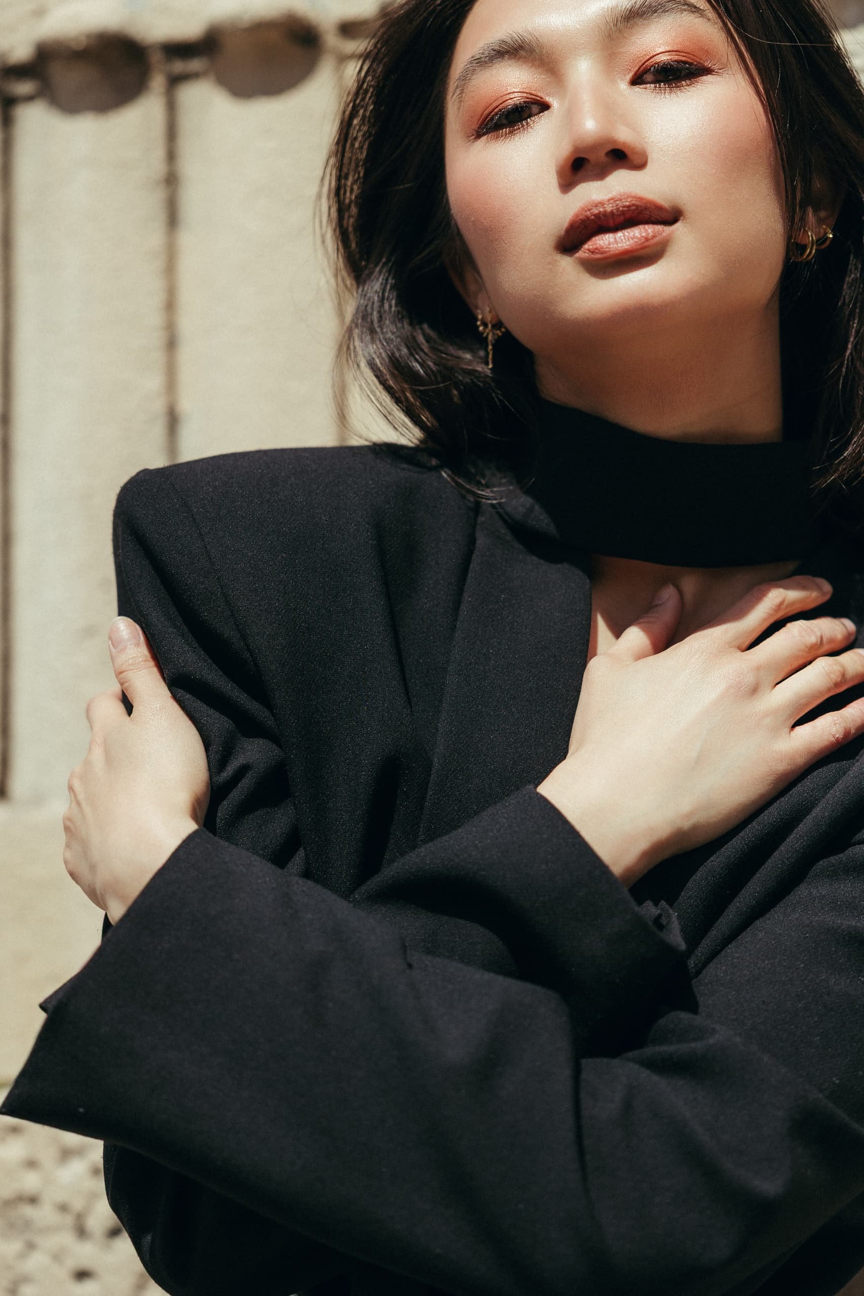 Fashionable woman in black blazer posing confidently in sunlight.