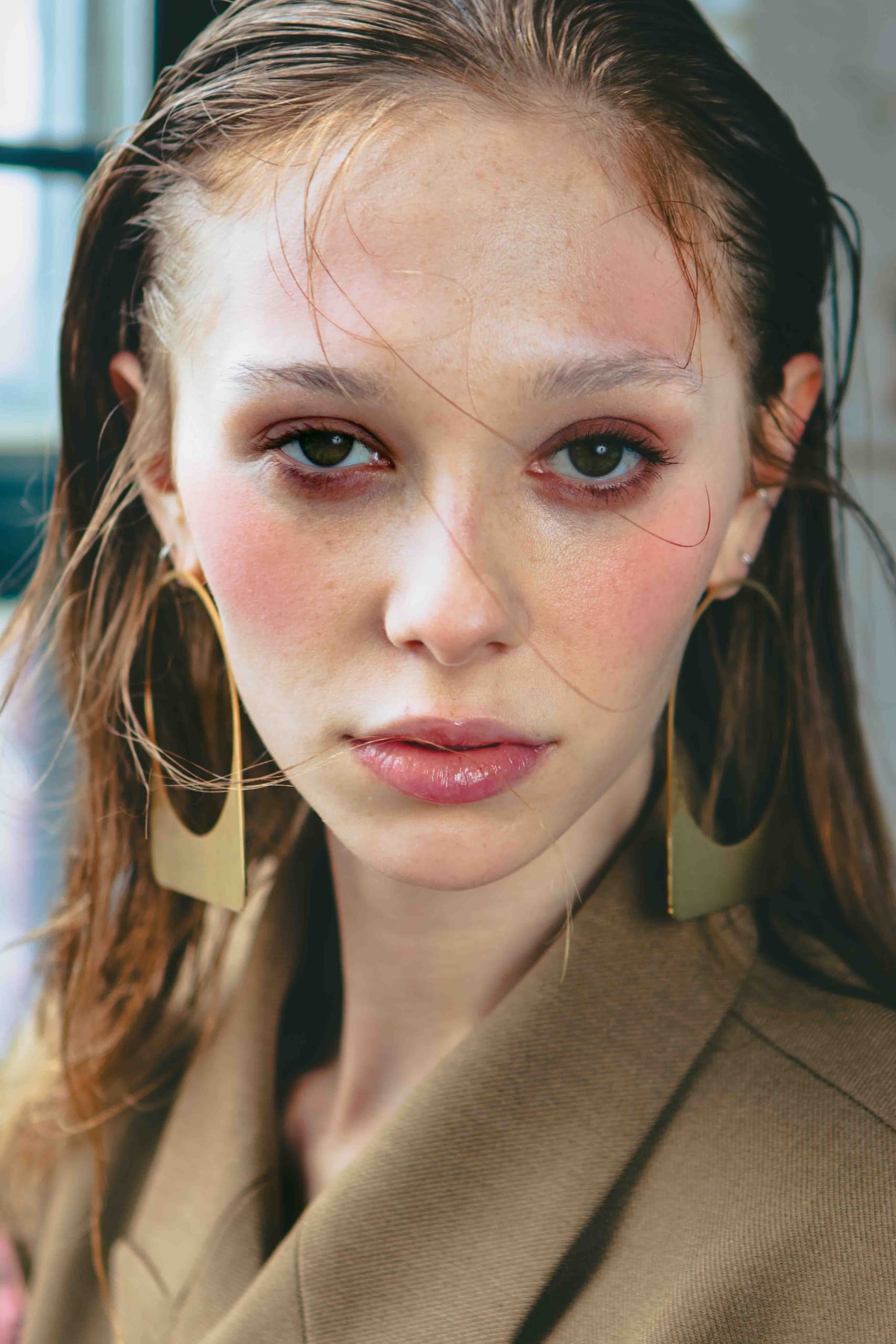 Close-up portrait of a woman with statement earrings and natural makeup.