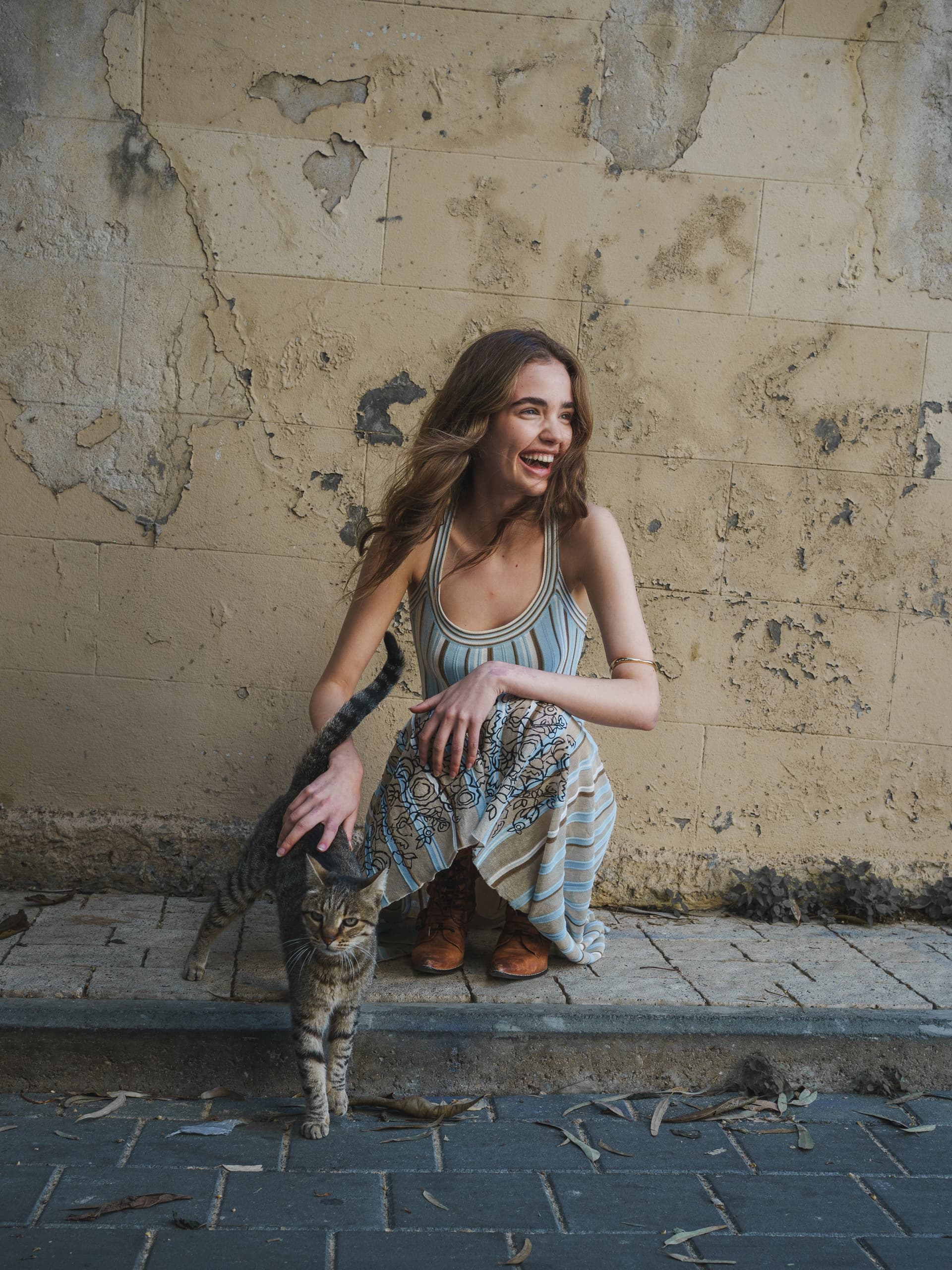 Smiling woman petting a cat against a rustic wall background.