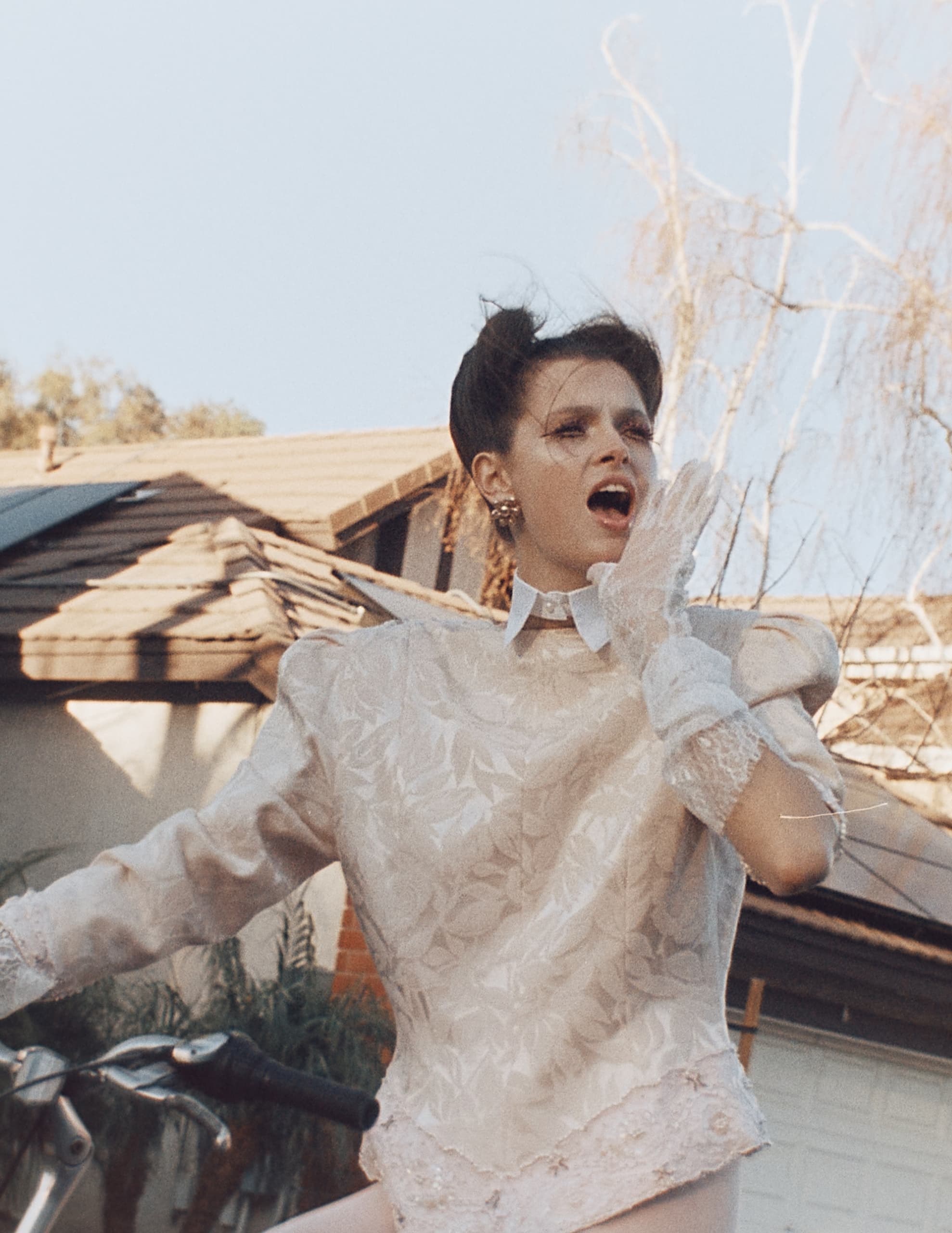 Person in vintage attire reacts dramatically outdoors, standing by a bicycle.