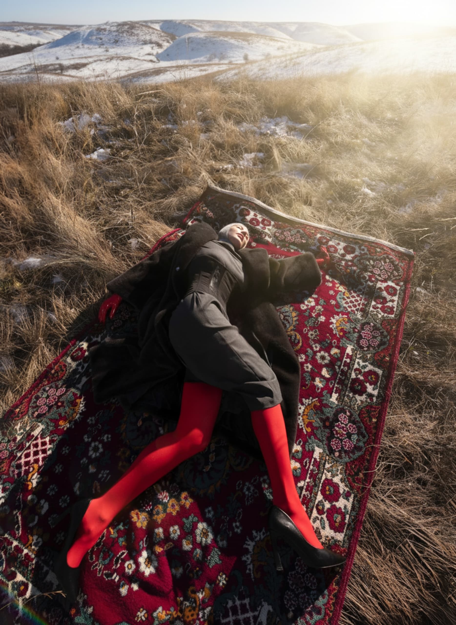 Person in red tights resting on ornate rug in a snowy landscape.