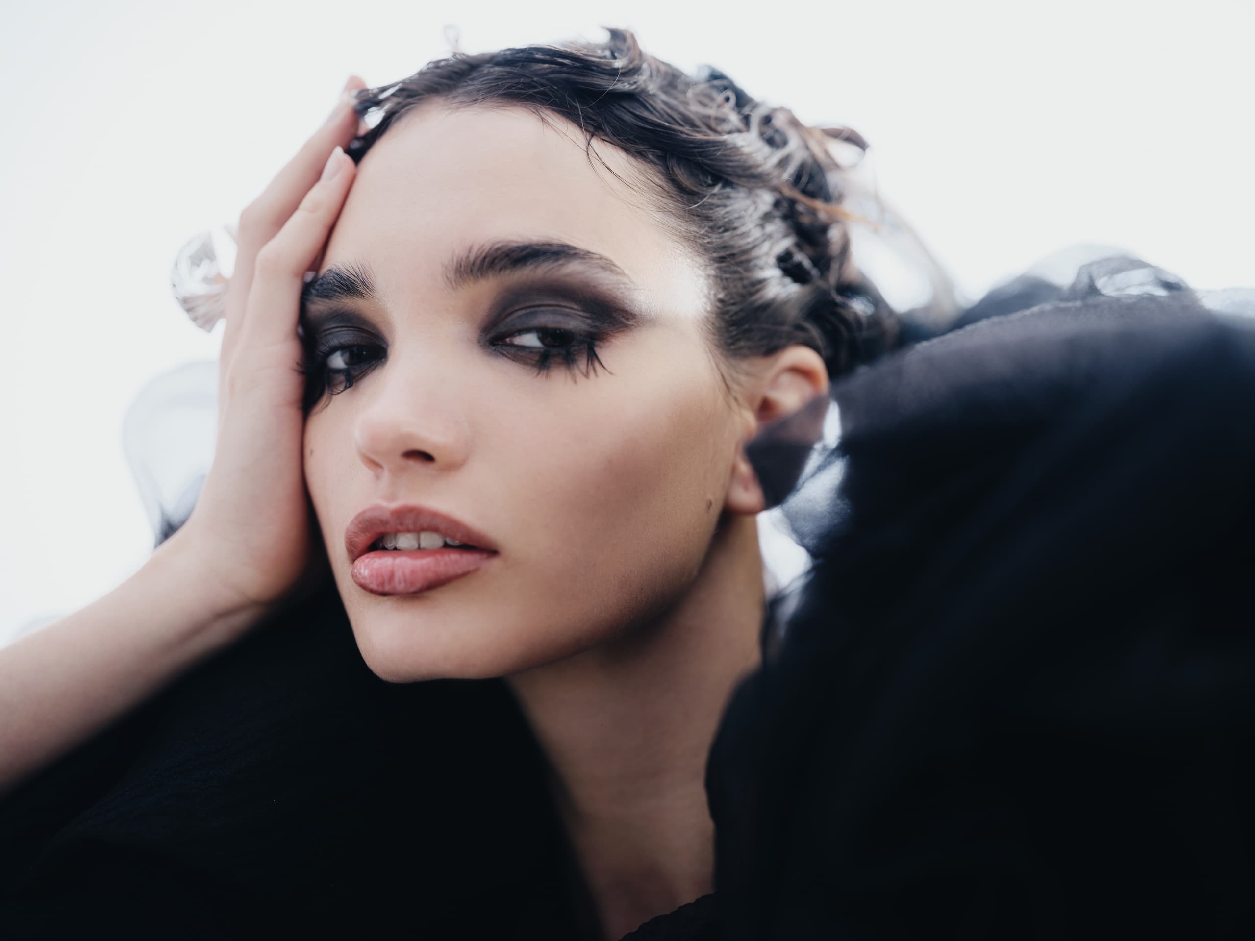 Woman with dramatic eye makeup and dark clothing, gazing intently.
