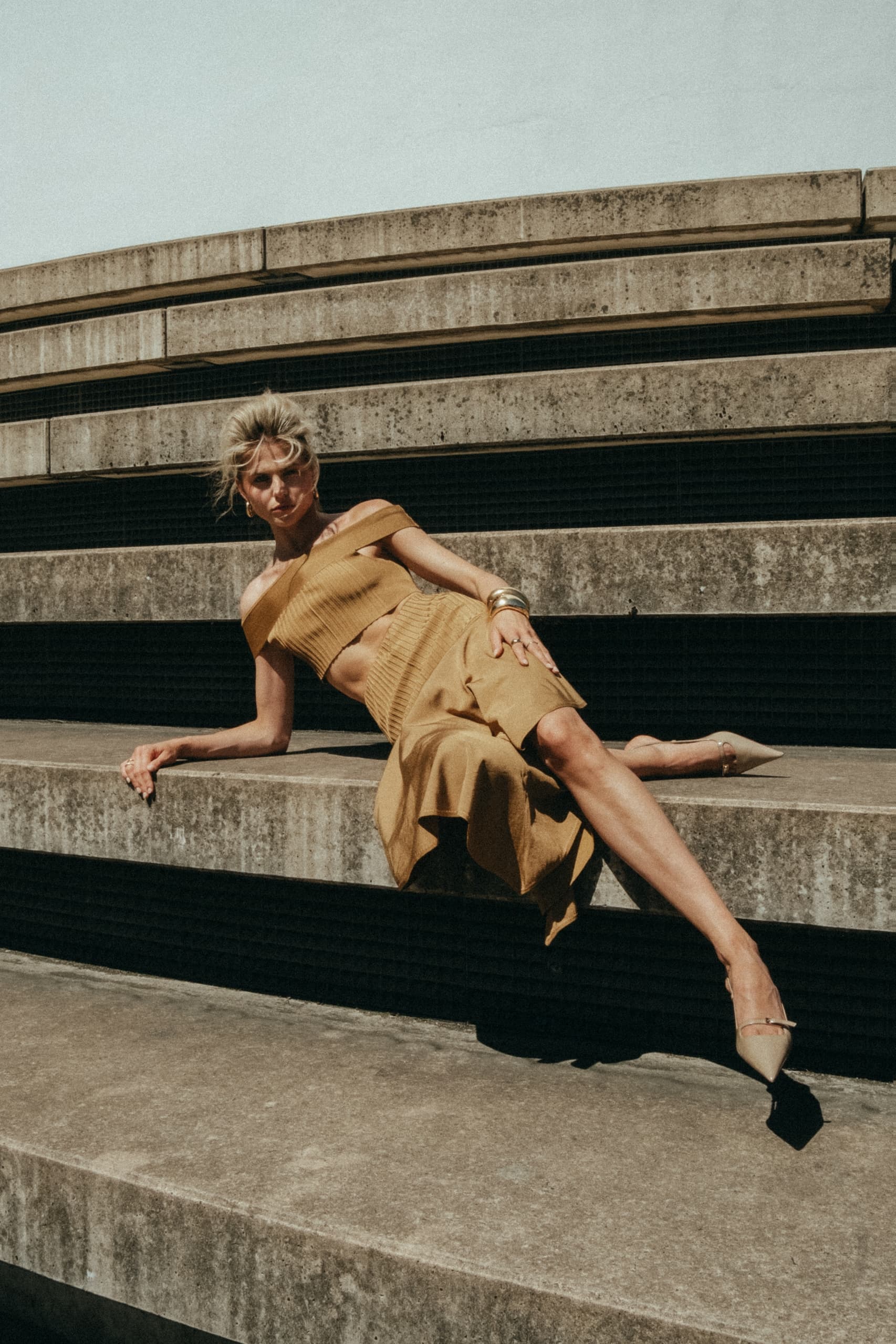 Woman in stylish beige outfit lounging on concrete steps.