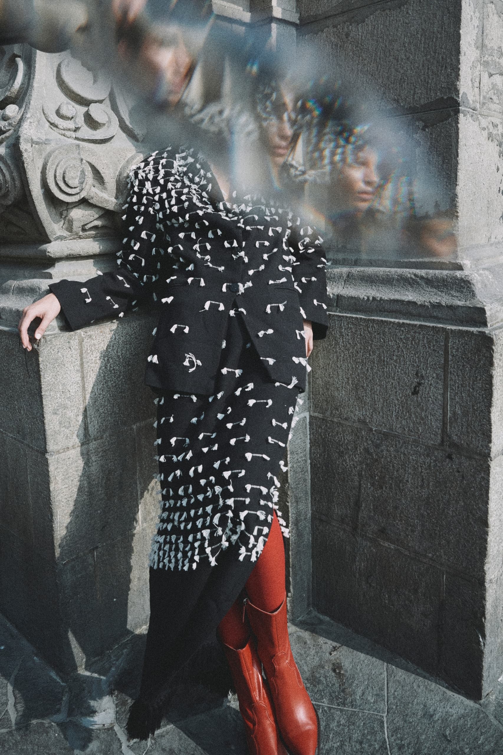Fashionable person in patterned coat with distortions near stone structure.