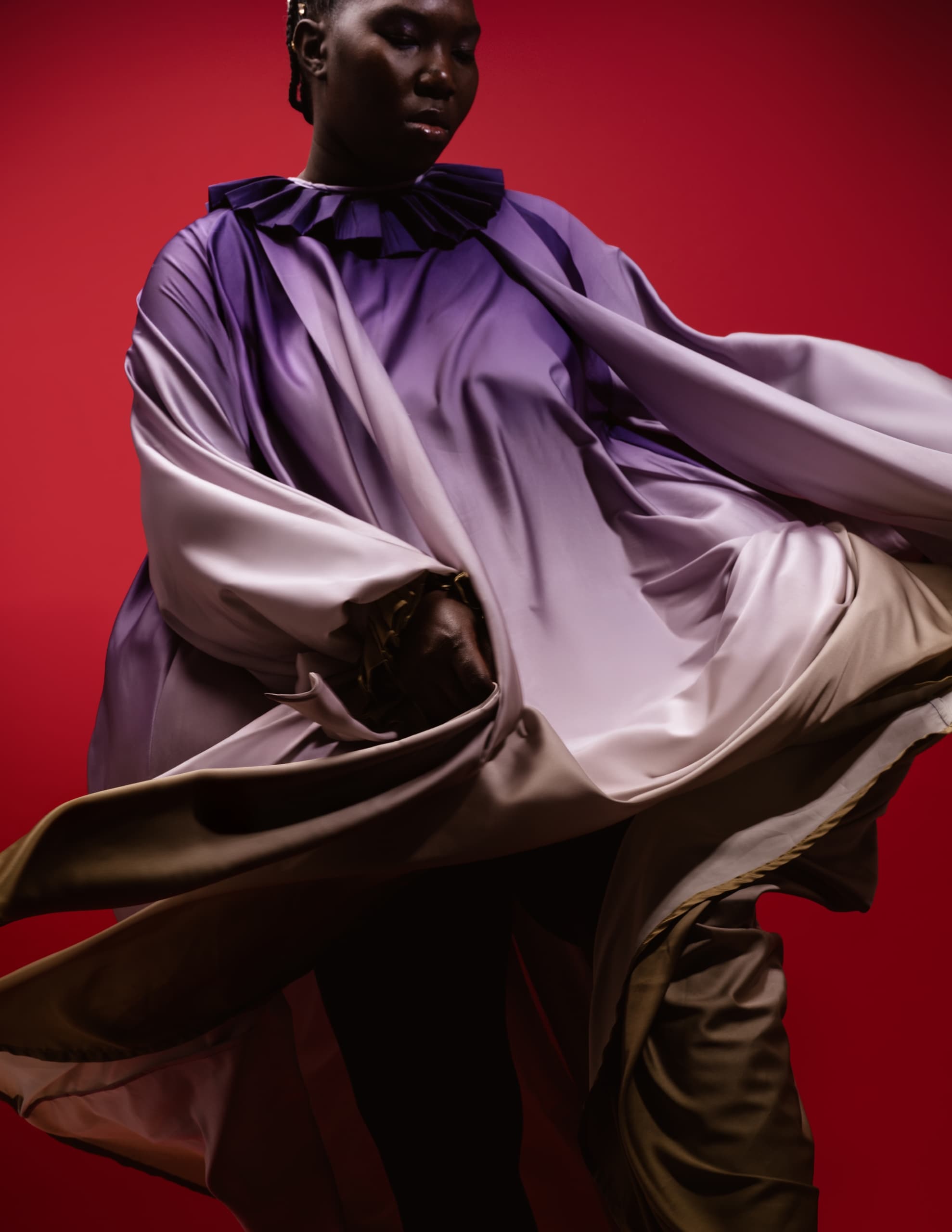 Person wearing flowing purple outfit in front of a vivid red background. Fashion style.