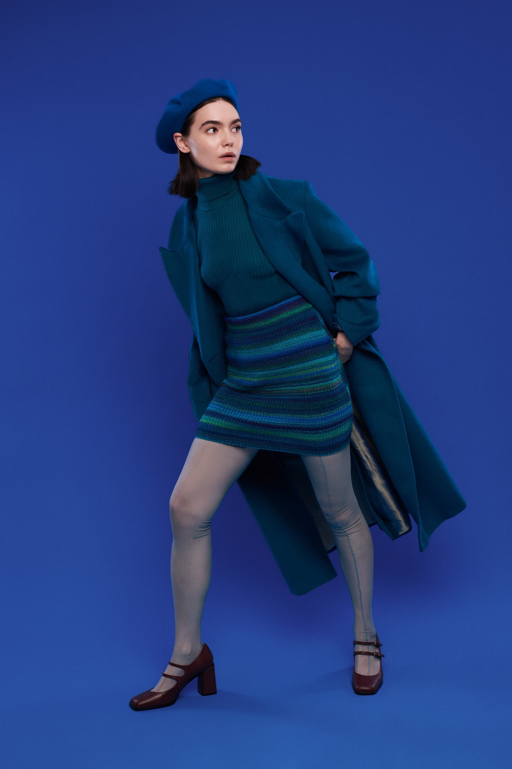 Fashionable woman in stylish blue outfit poses against blue background.