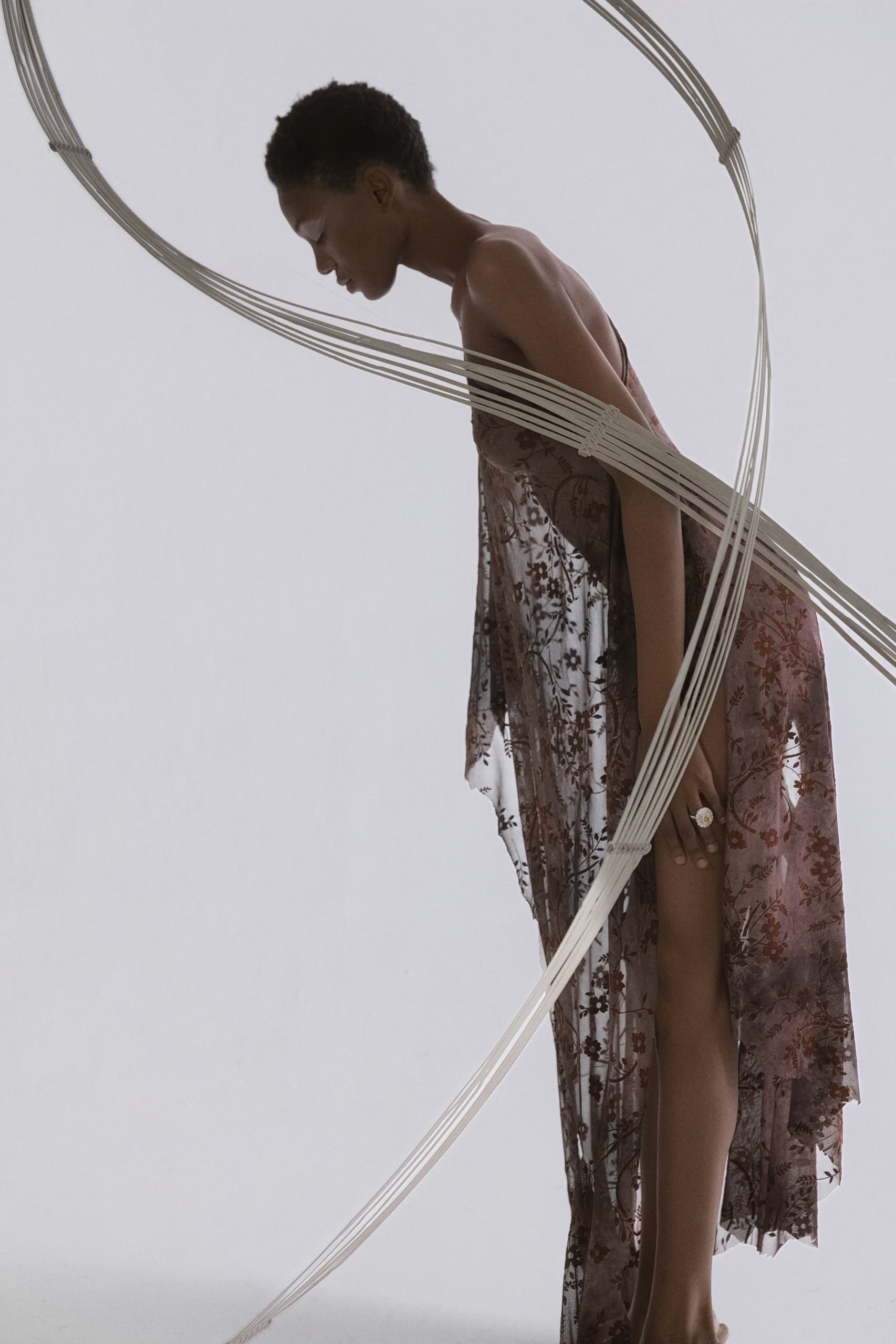 Model in floral dress artfully entwined in white hoops, contemporary fashion photography.