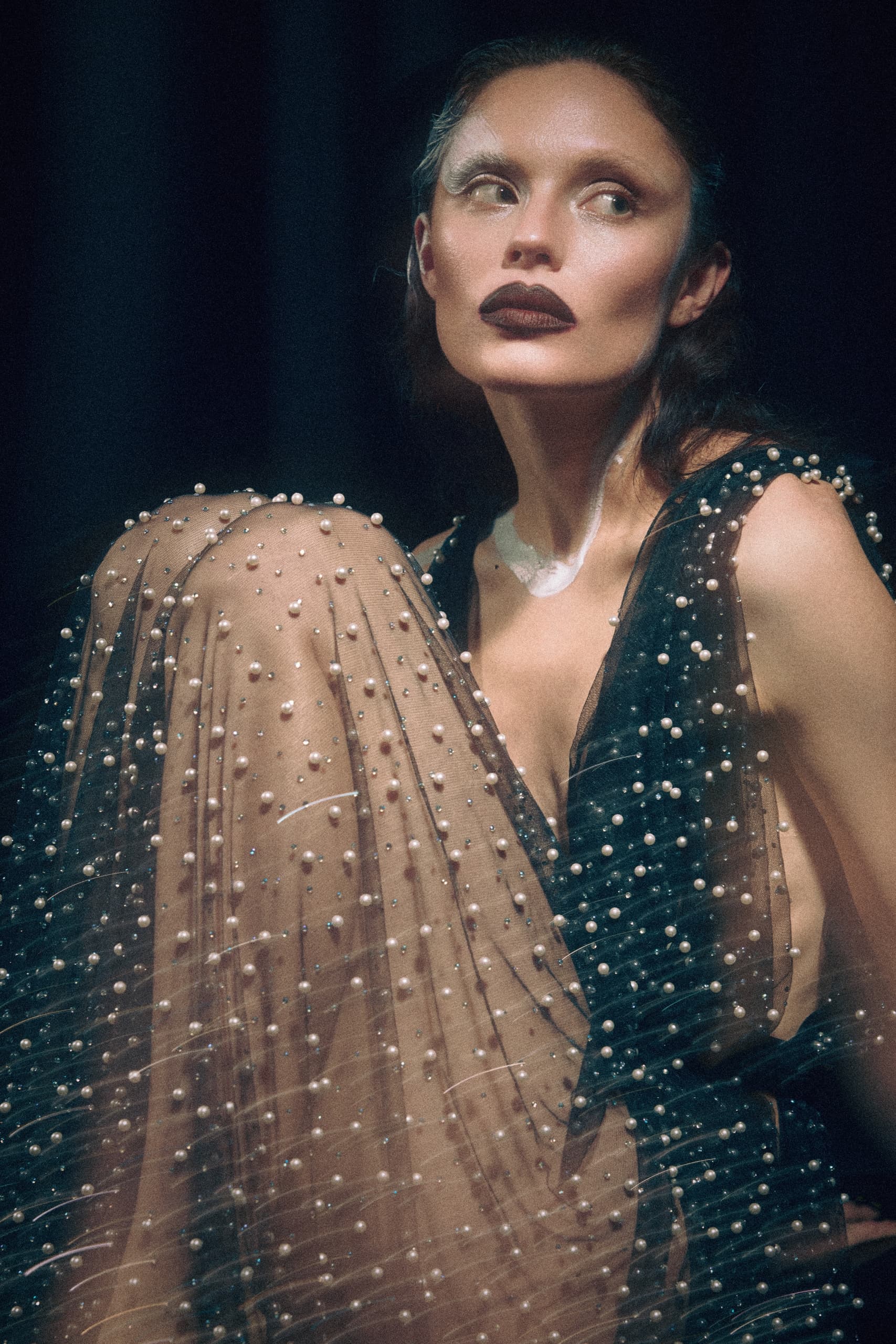 Elegant woman in a pearl-studded gown gazes thoughtfully.