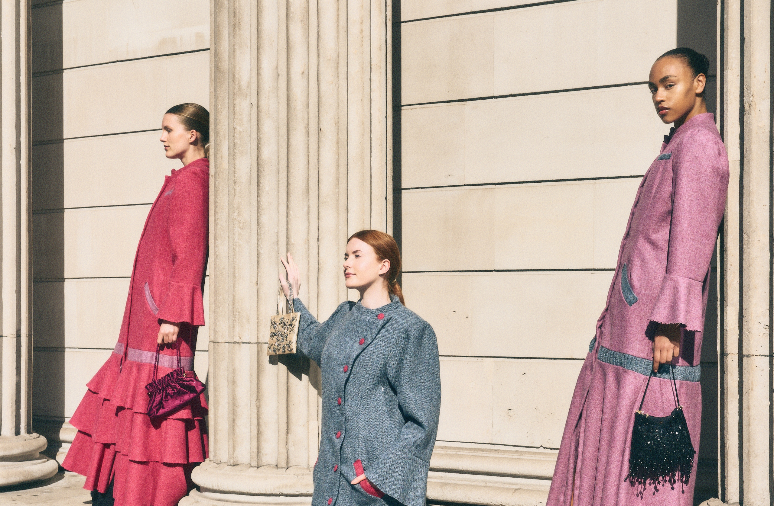 Models in stylish coats with handbags at architectural columns.