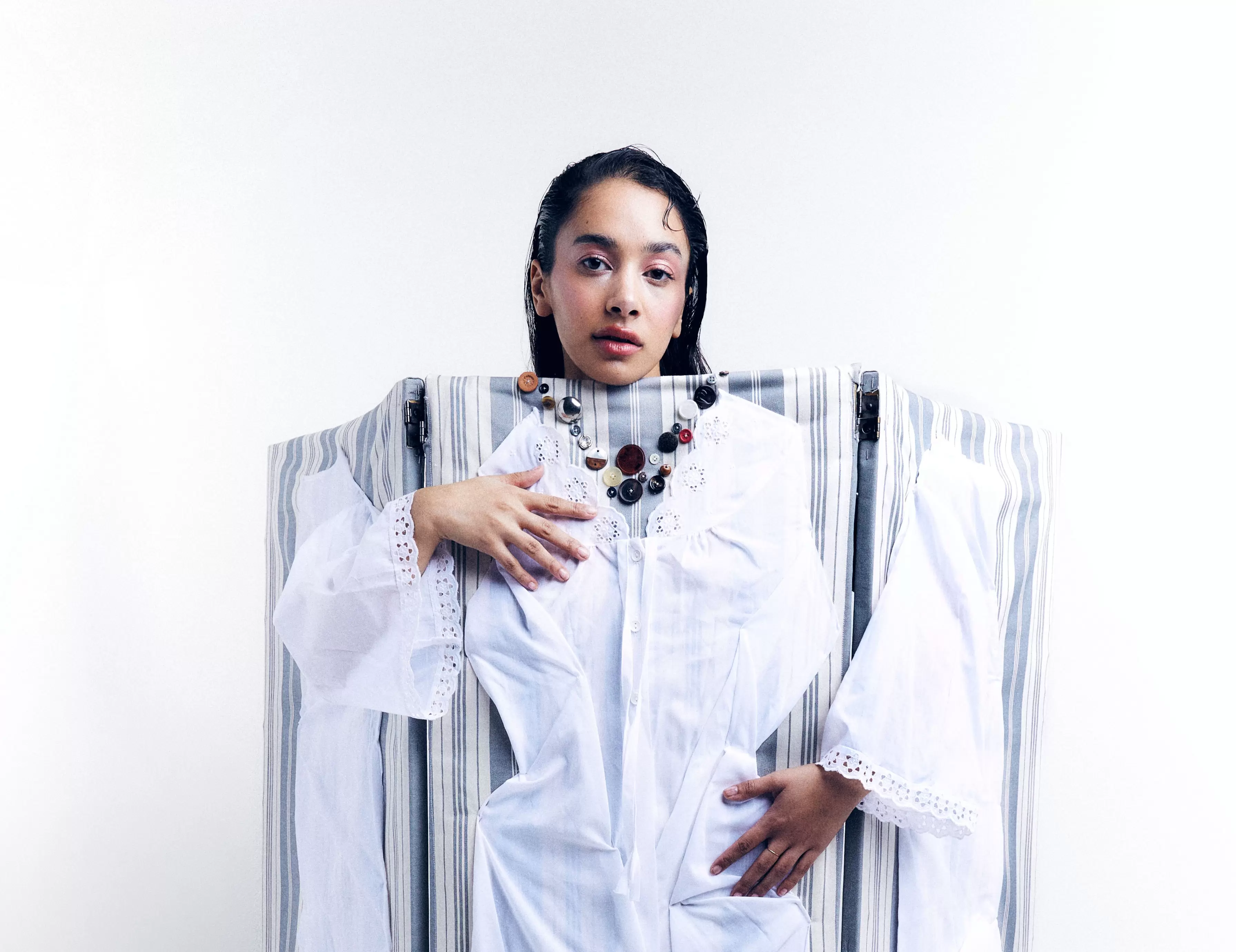 Woman in artistic white dress, standing against striped abstract background.