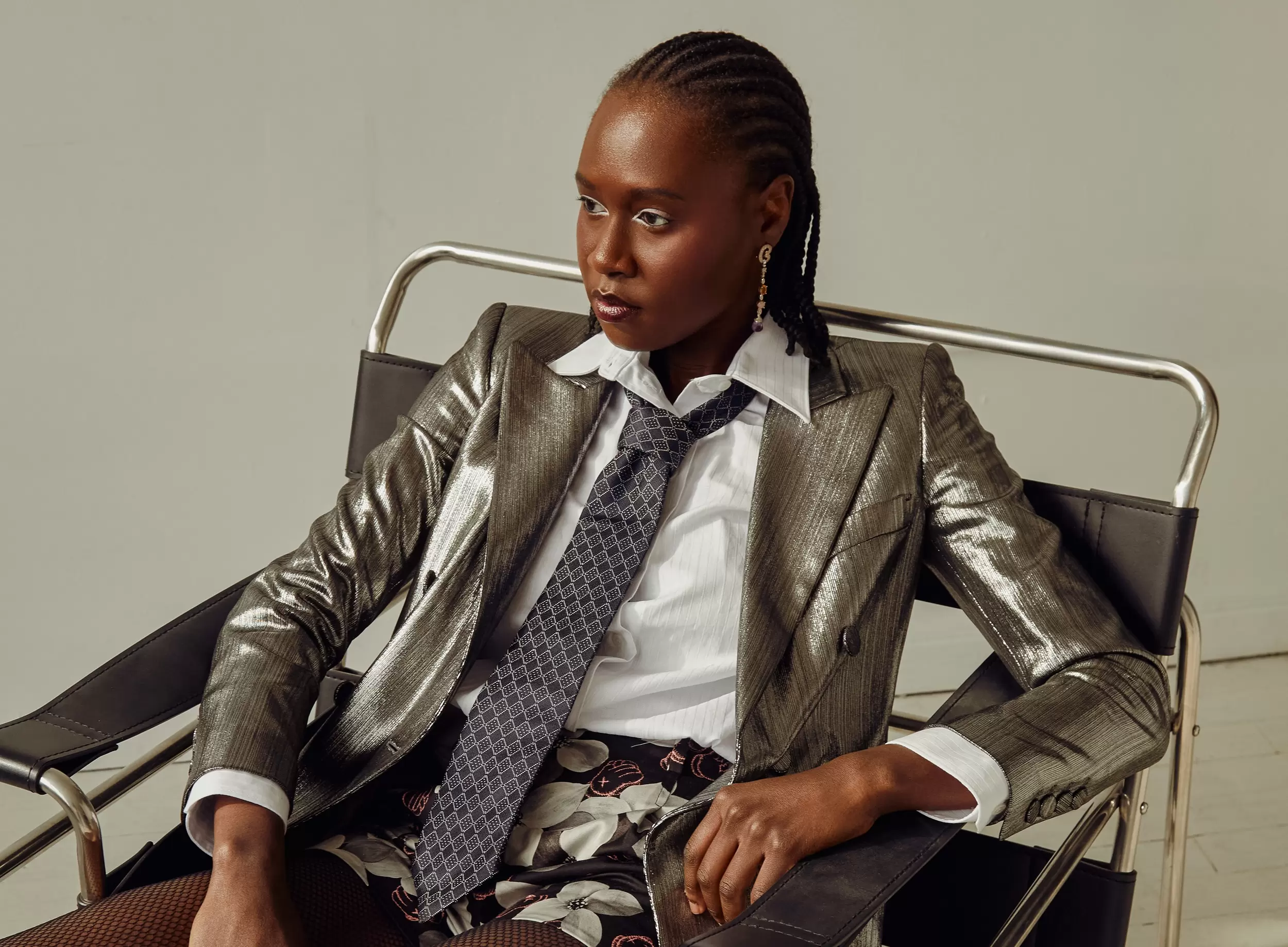 Stylish individual seated in a metallic jacket and tie, exuding confidence.