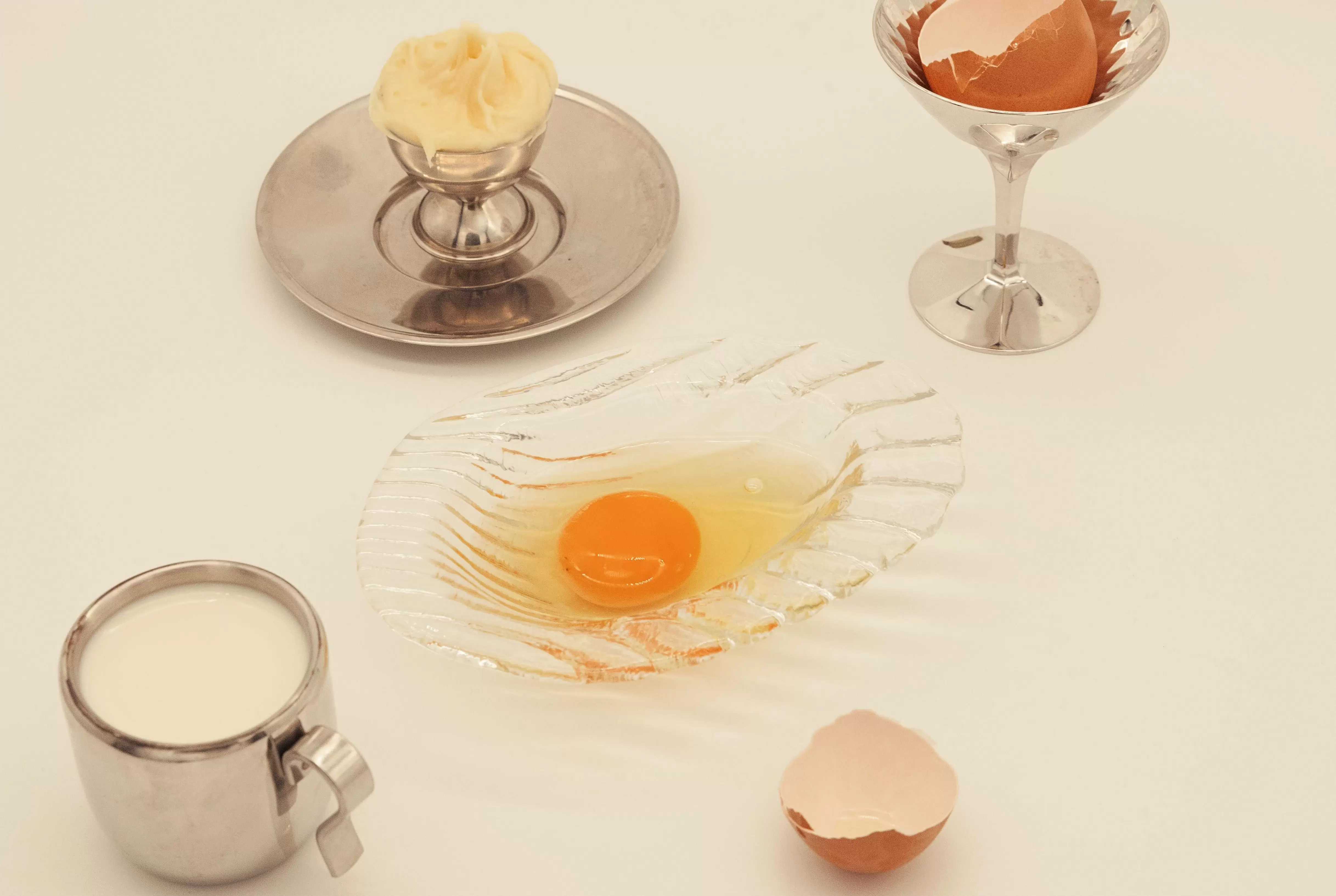 Raw egg, shell, milk, and butter on silver platters for a minimalist culinary setup.