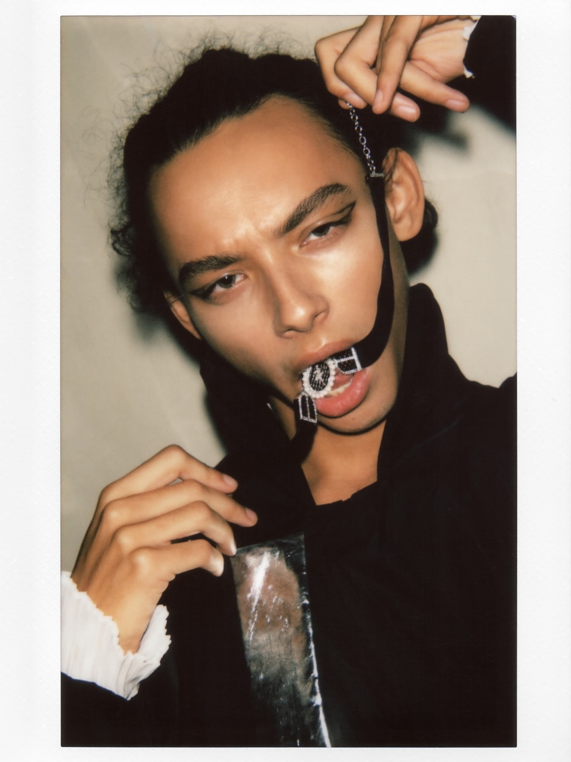 Creative fashion portrait with bold eyeliner, holding a bejeweled chain in mouth.