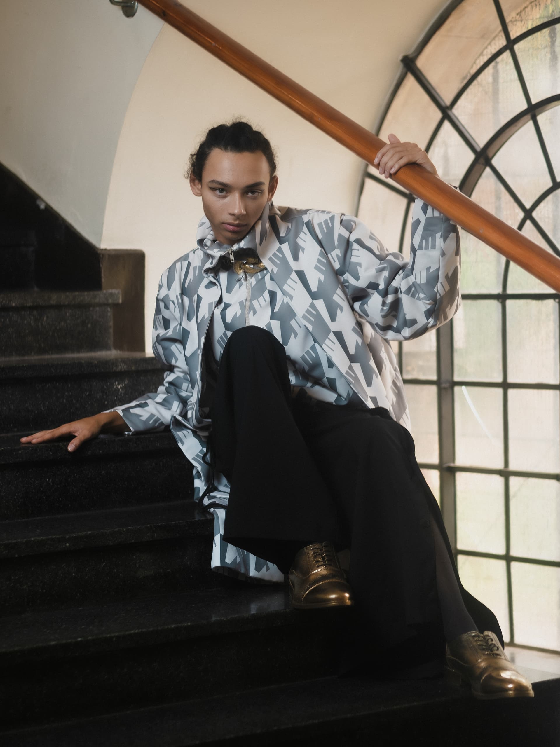 Fashionable person posing on staircase in a stylish geometric-patterned outfit.
