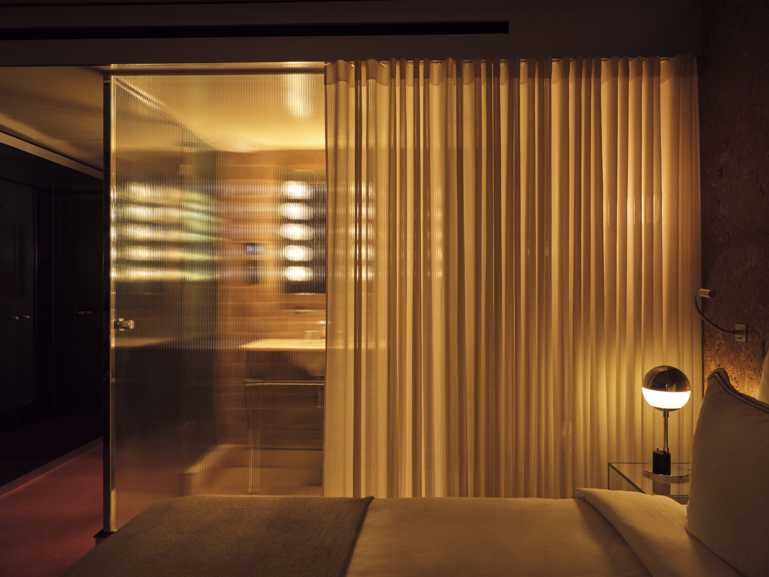 Modern hotel room with dim lighting, glass divider, and cozy ambiance.