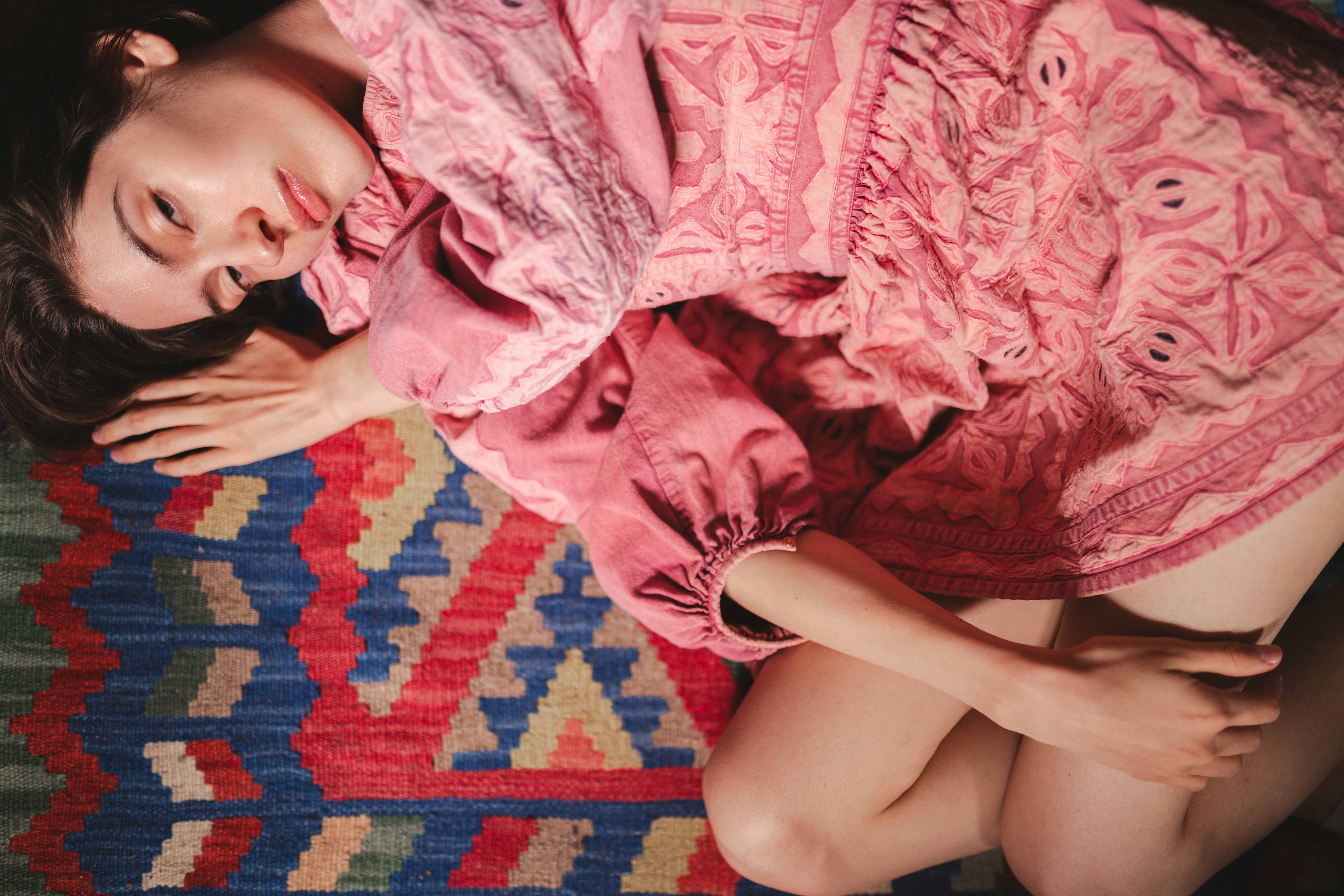 Woman in pink dress lying on colorful geometric-patterned rug.