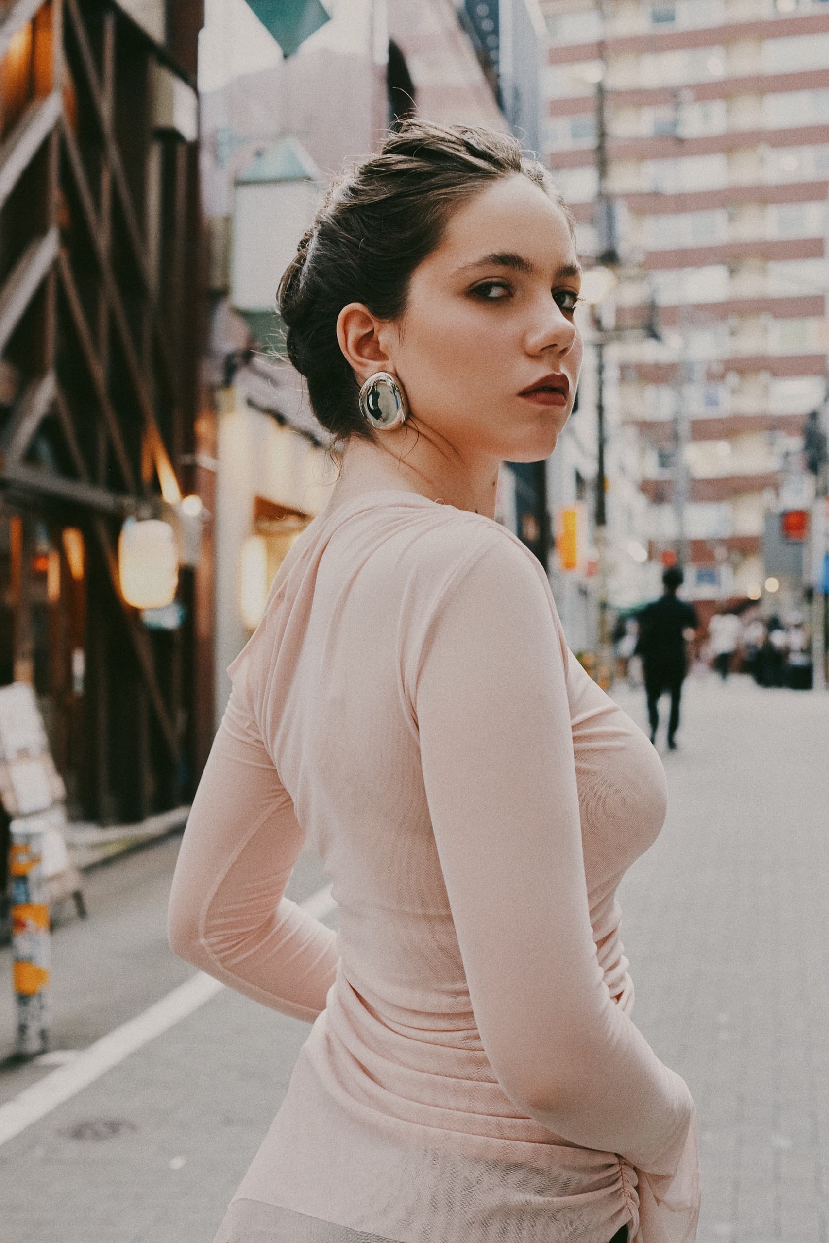 Stylish woman in a city street wearing elegant earrings and pink blouse.