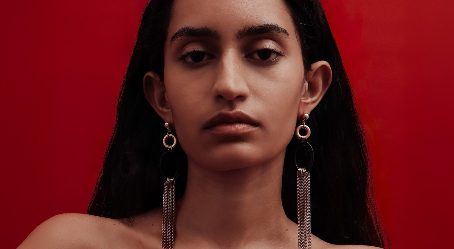 Portrait of woman with long earrings against a vibrant red background.