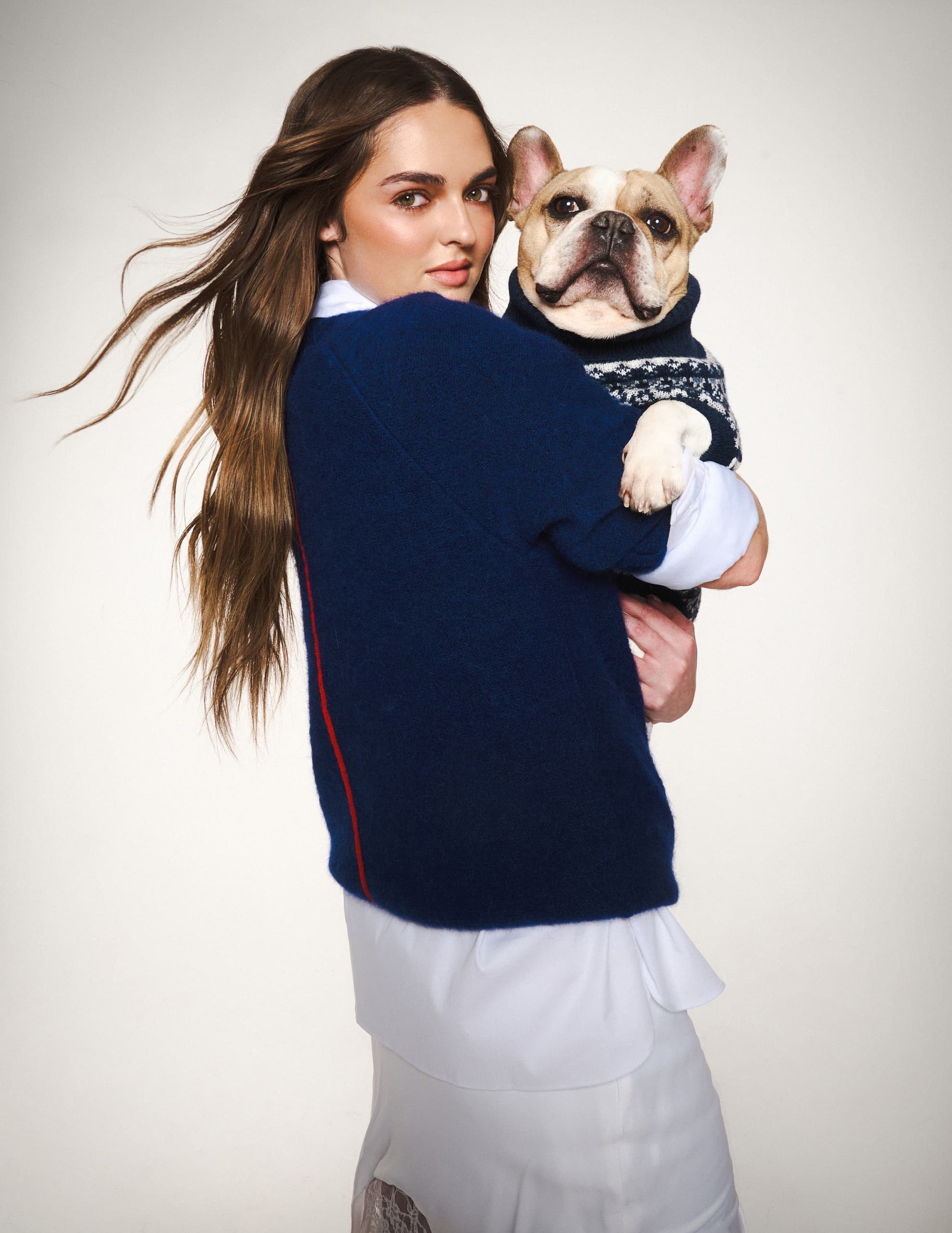 Woman holding French bulldog in blue sweater, studio portrait.