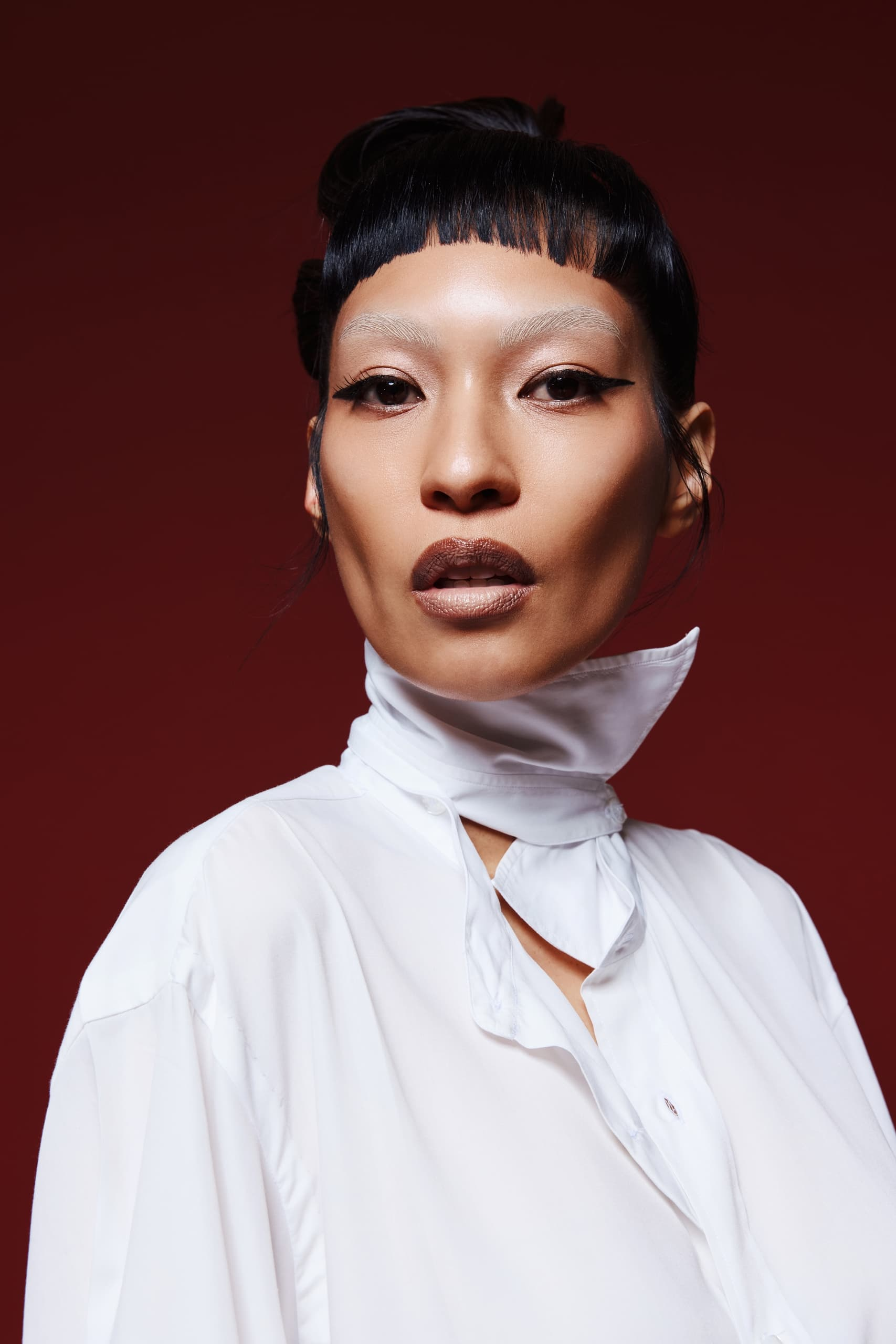 Fashion portrait of individual in white blouse on a red background, bold makeup.