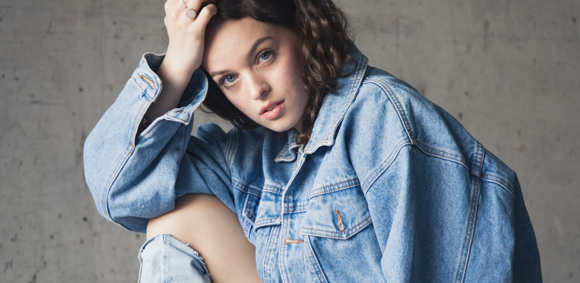 Person in denim jacket posing against a neutral background.