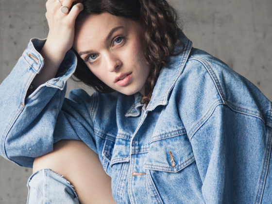 Person in denim jacket posing against a neutral background.