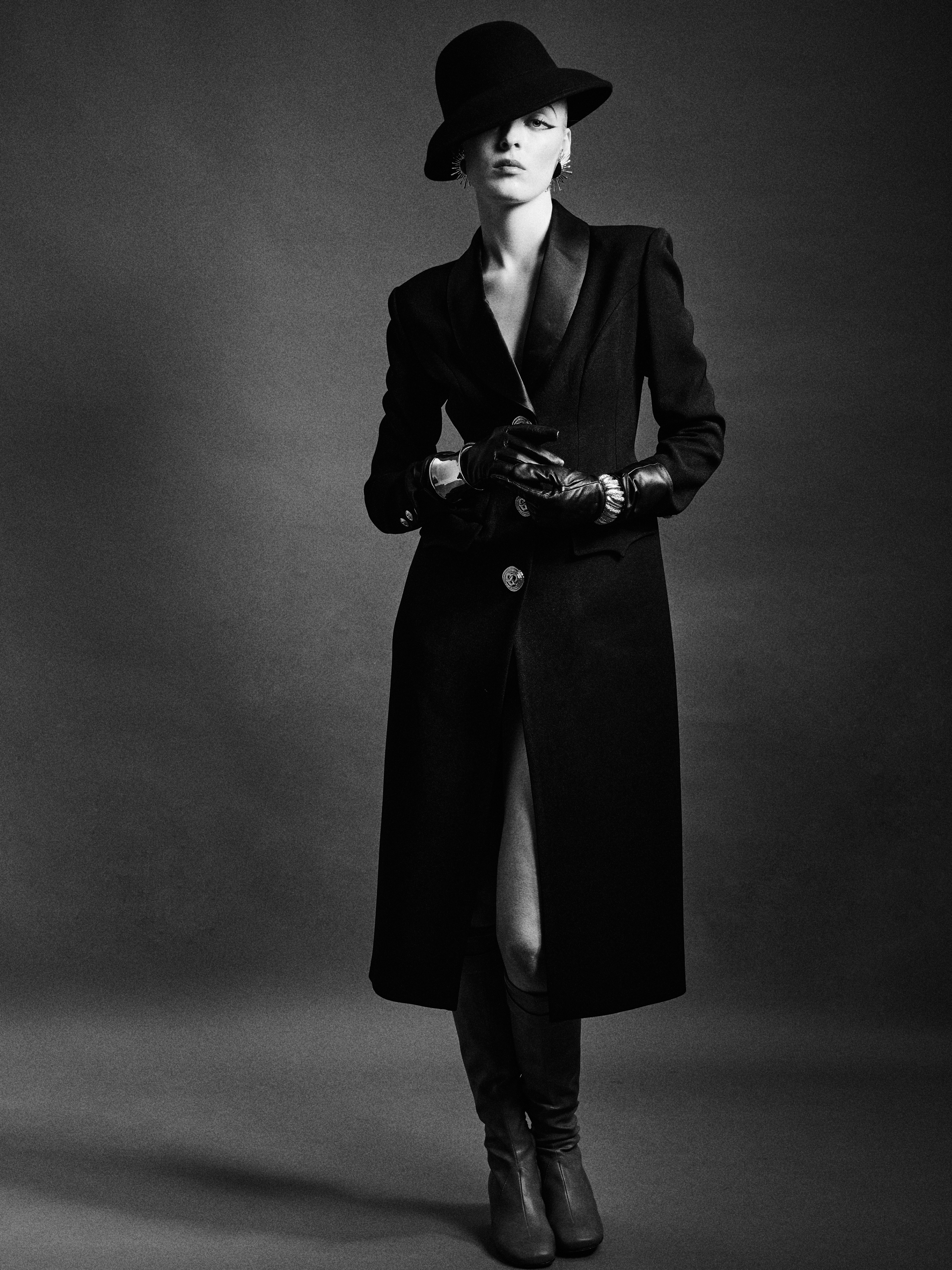 Fashionable woman in black coat and hat, striking pose in black and white style.