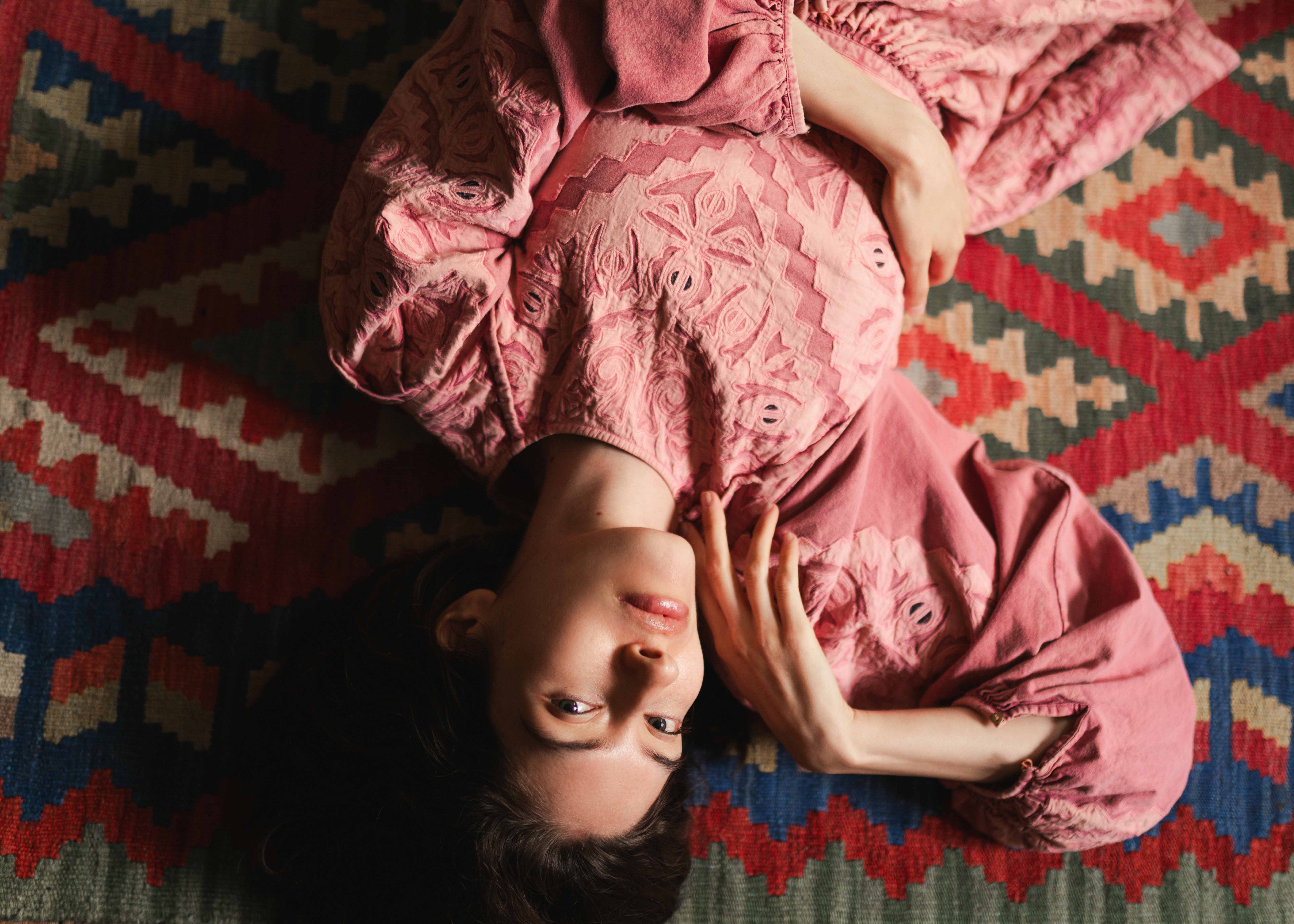 Woman in embroidered pink dress lying on a colorful geometric-patterned rug.