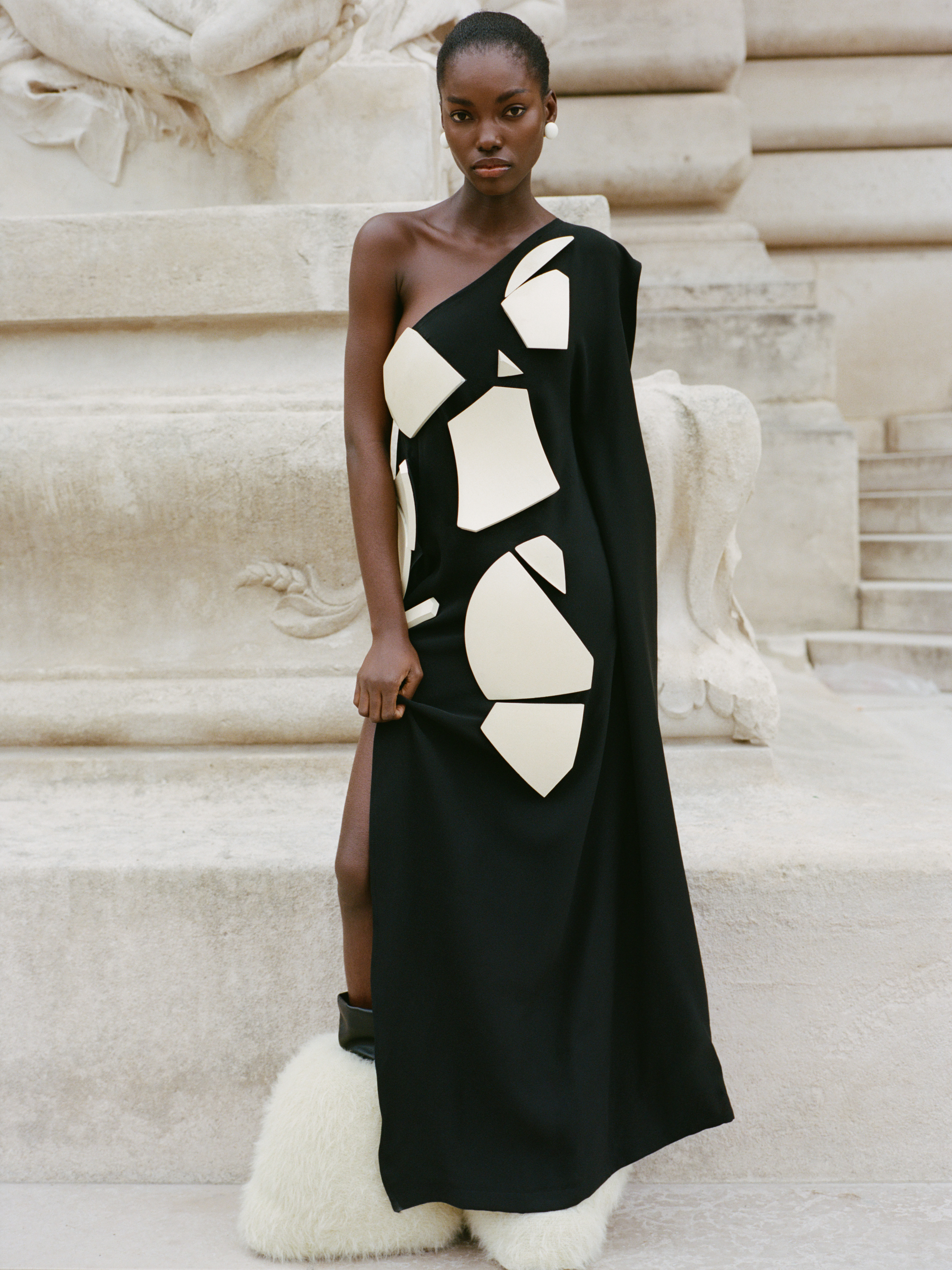 Model in a stylish black gown with geometric shapes and unique footwear.