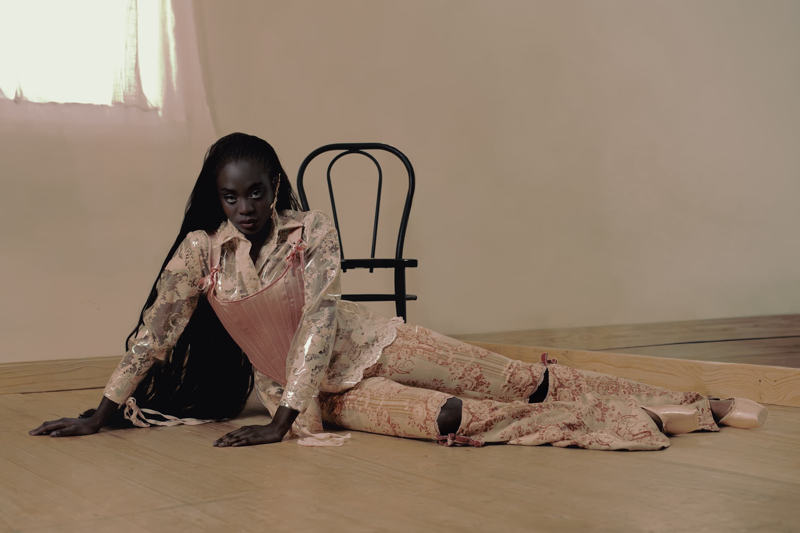 Model in floral fashion on wooden floor with chair backdrop.