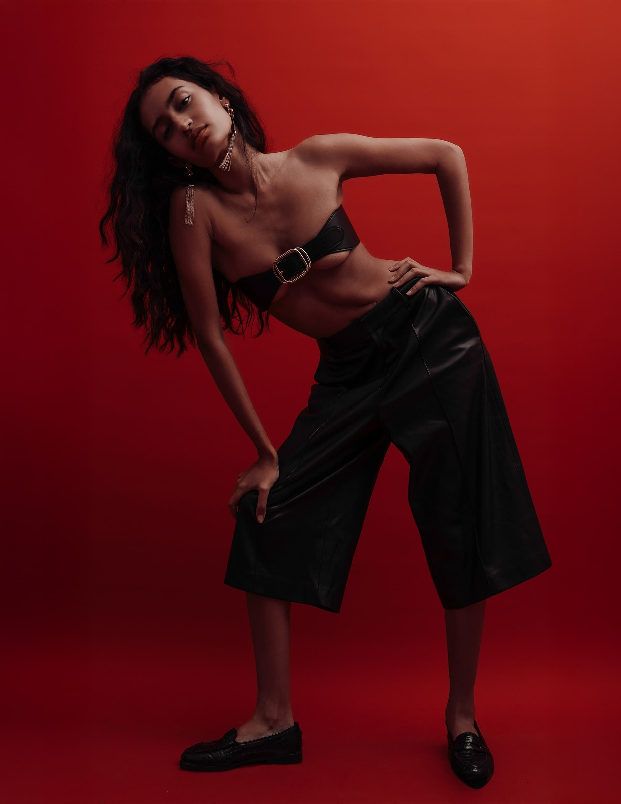 Fashion model poses in edgy black attire on a vibrant red background.