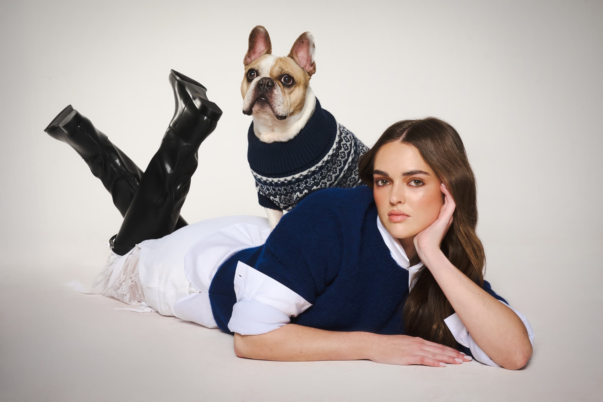 Model in stylish outfit with French Bulldog in sweater on a studio floor.