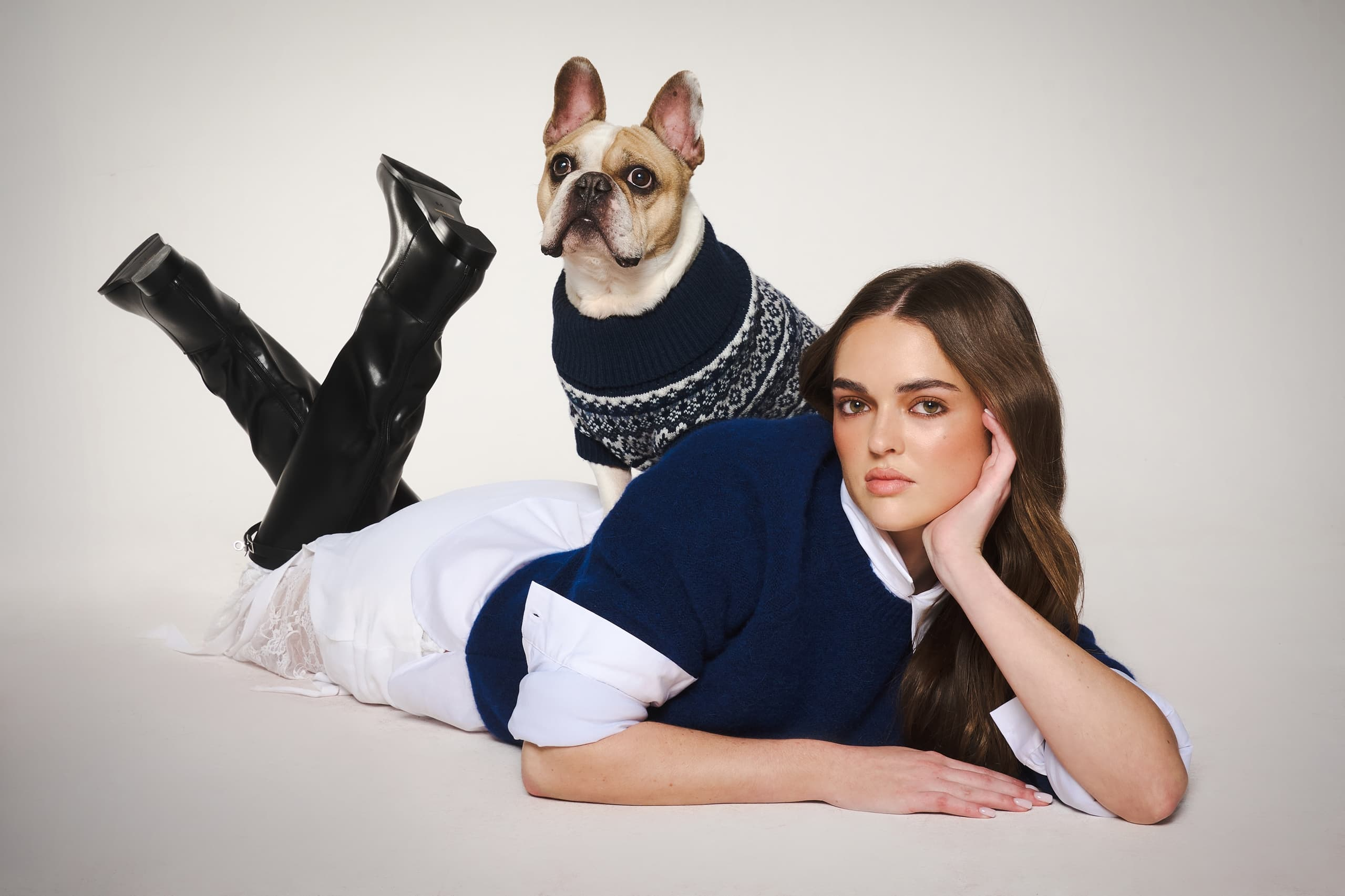 Model in stylish outfit with French Bulldog in sweater on a studio floor.