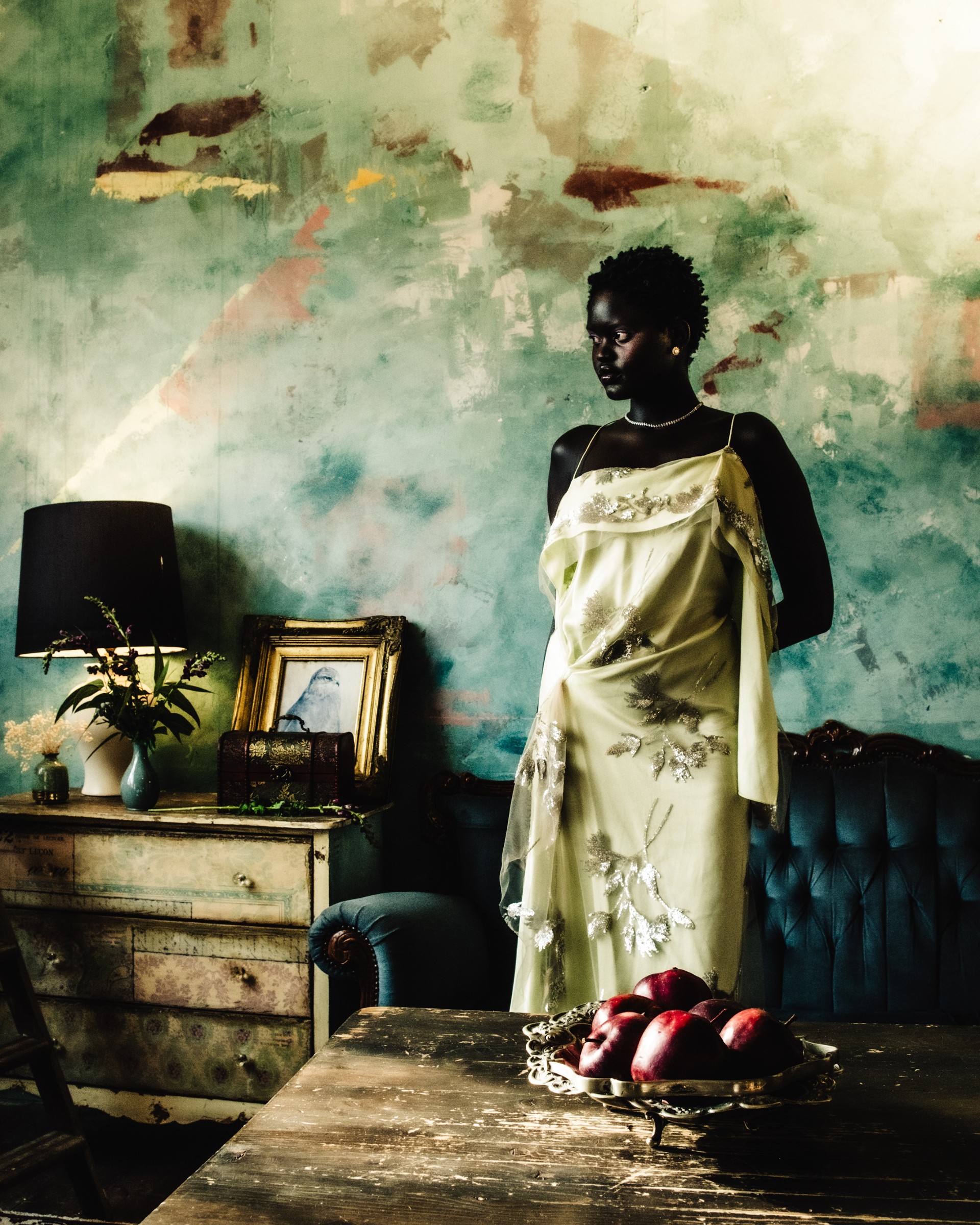 Elegantly dressed woman in vintage room with apples on table.