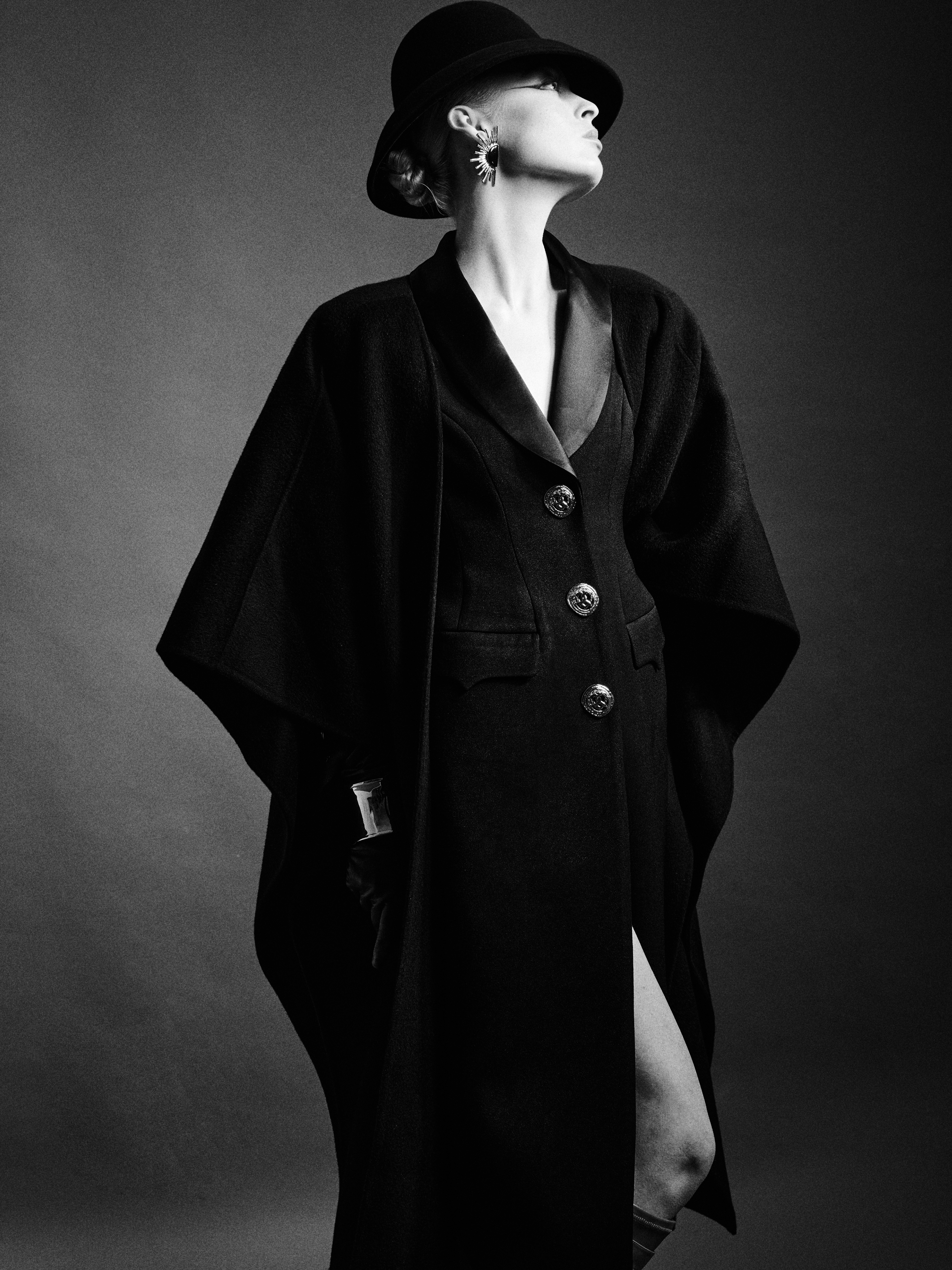 Elegant woman in black overcoat and hat, striking a stylish vintage pose.