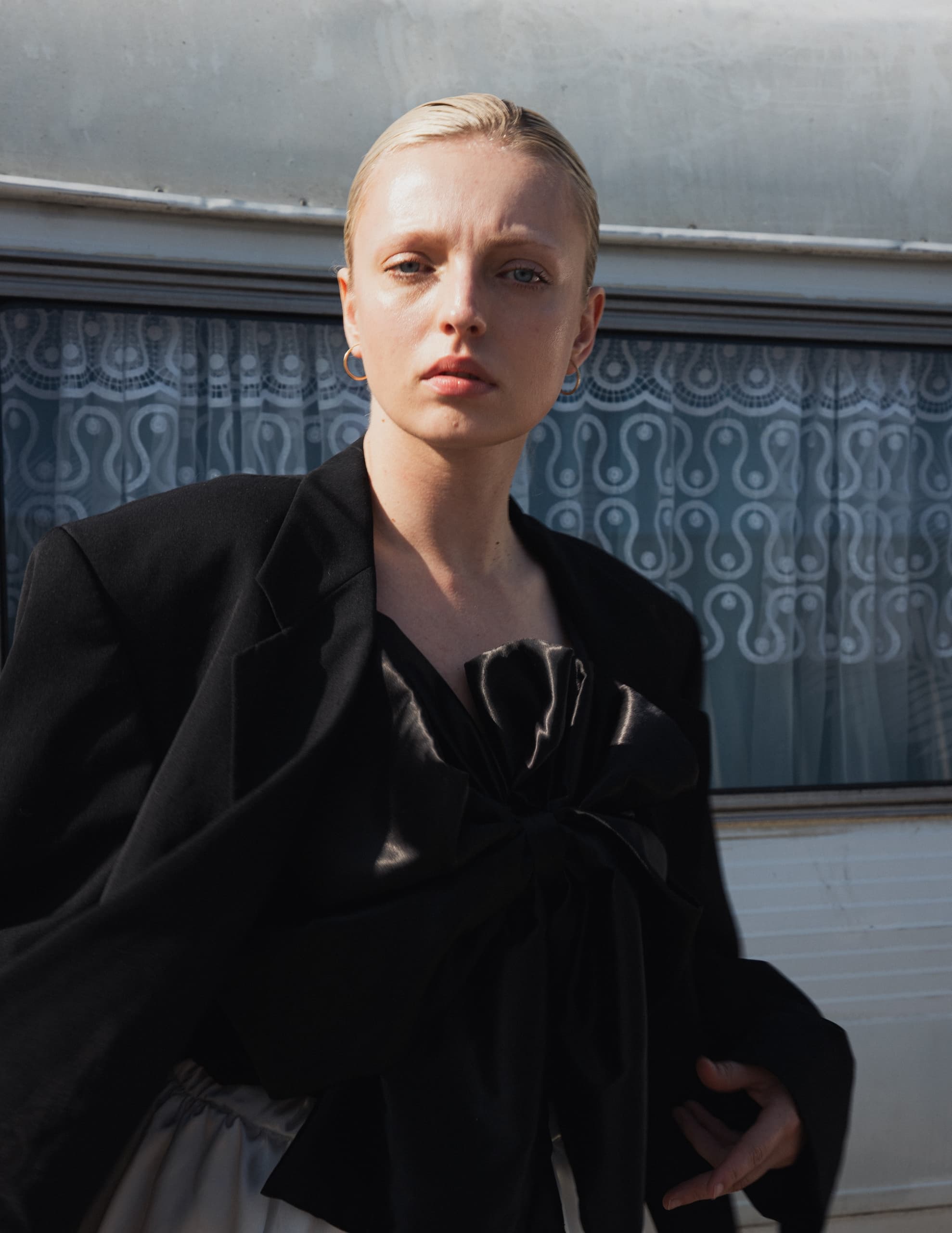 Person in elegant black outfit standing by a decorative window.