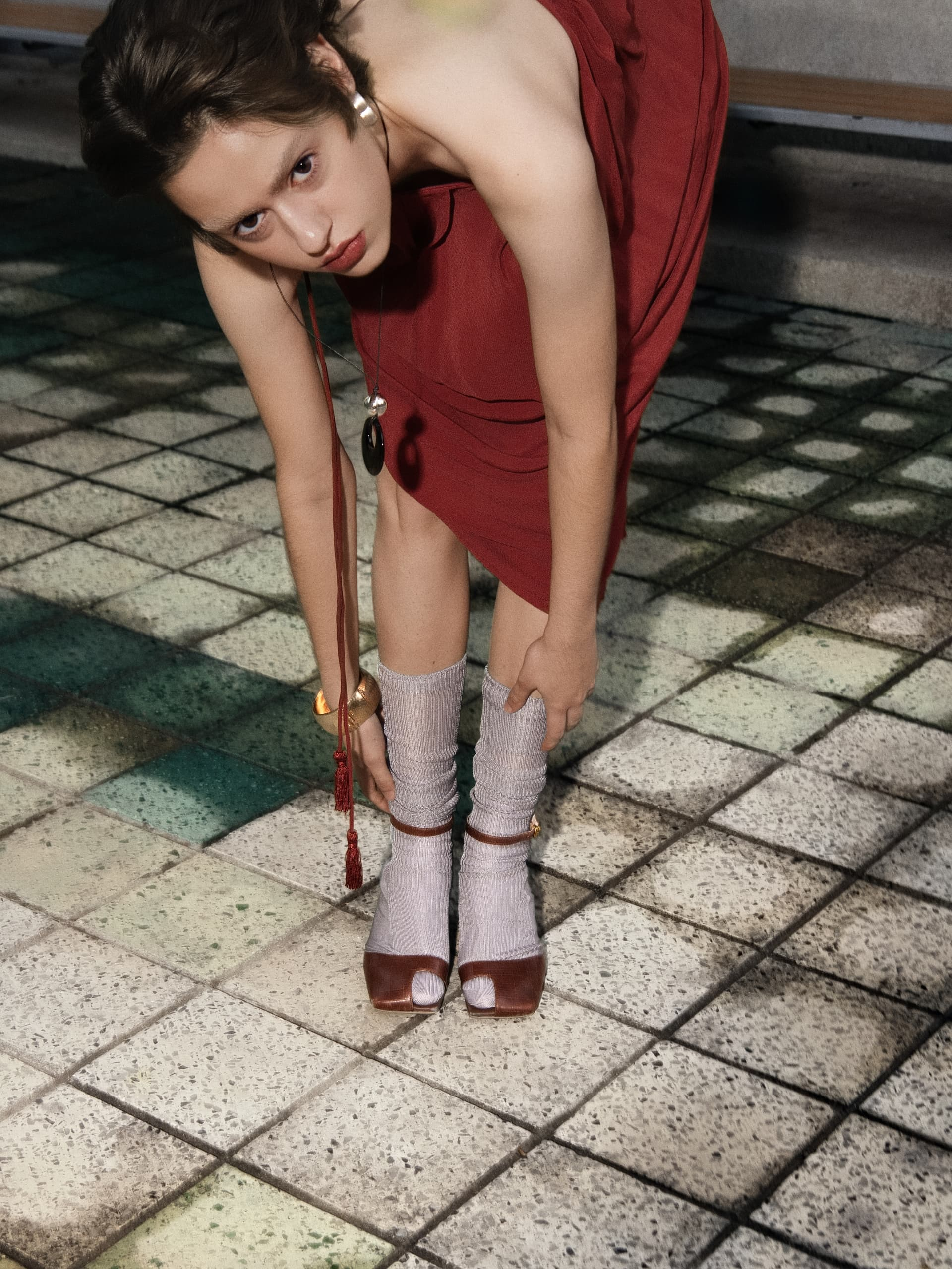 Person bending in red dress with open-toed shoes on a tiled floor.