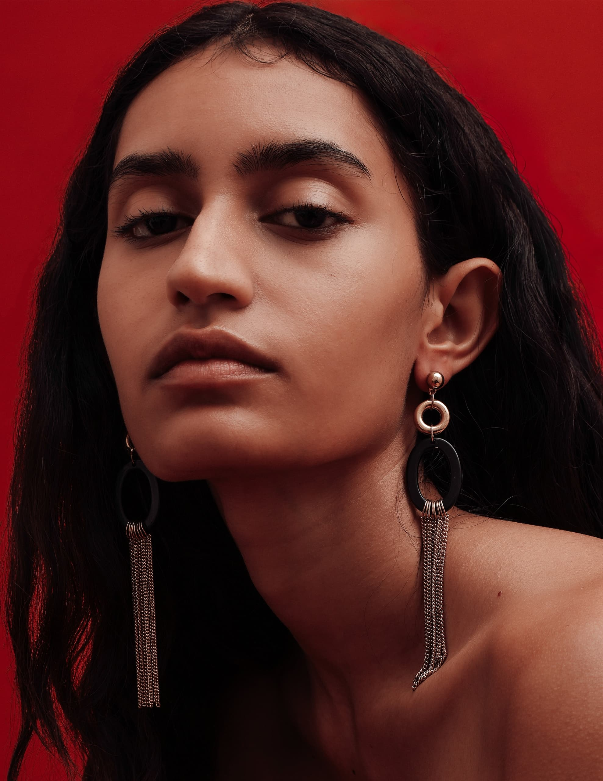 Woman with bold earrings, red background, confident pose.