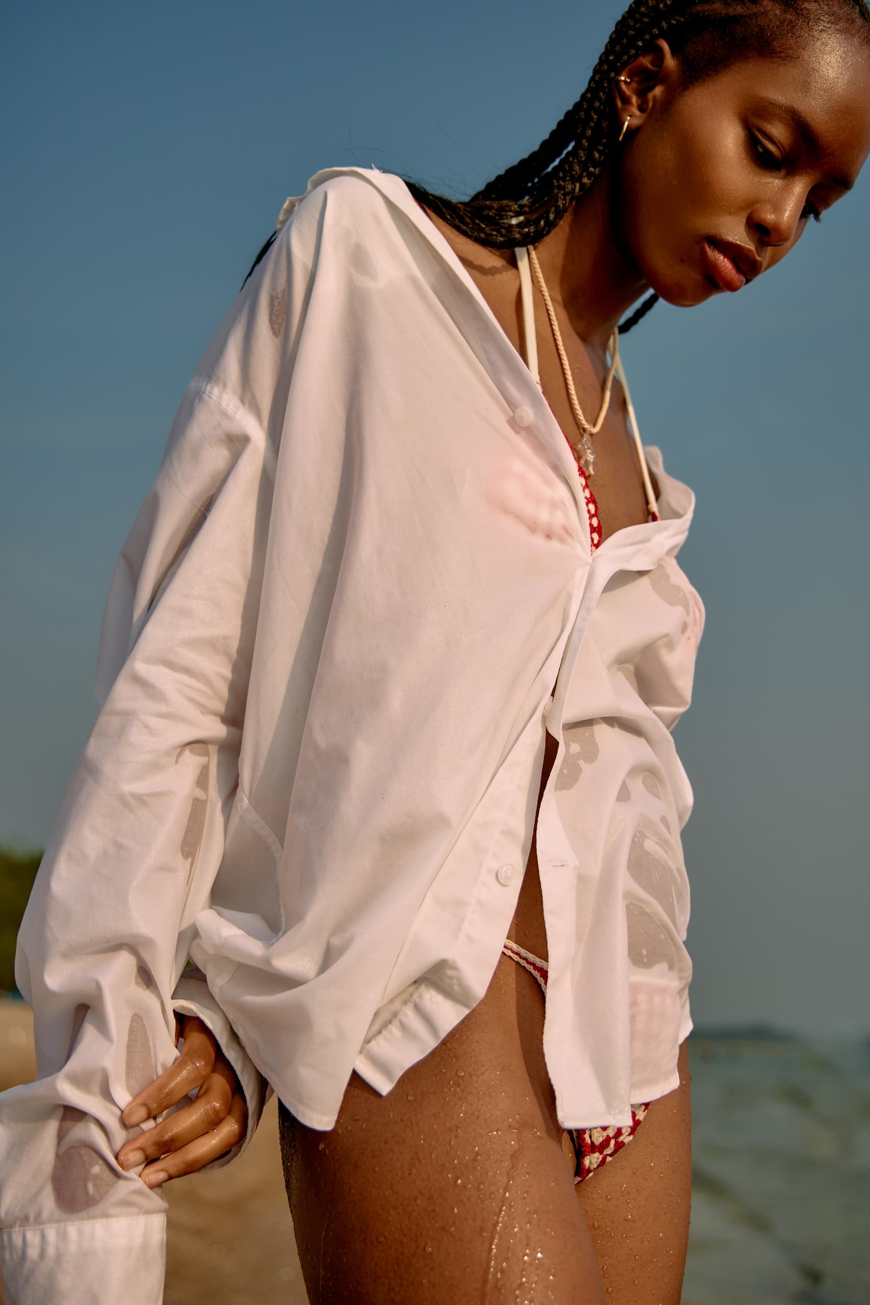 Person in white shirt and bikini at the beach with ocean in the background.