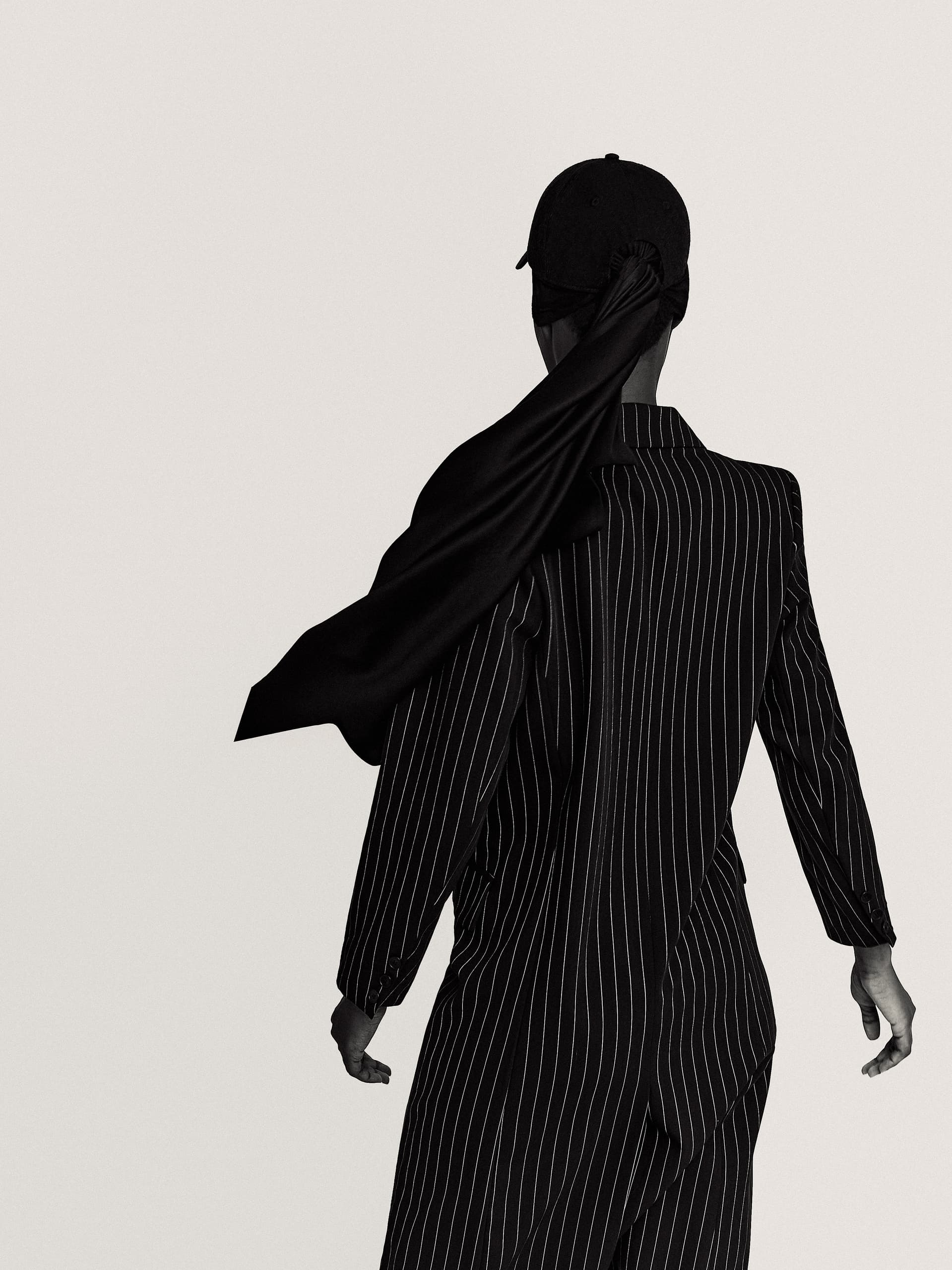 Person in a pinstripe suit with a long scarf blowing, back view. Minimalist fashion.