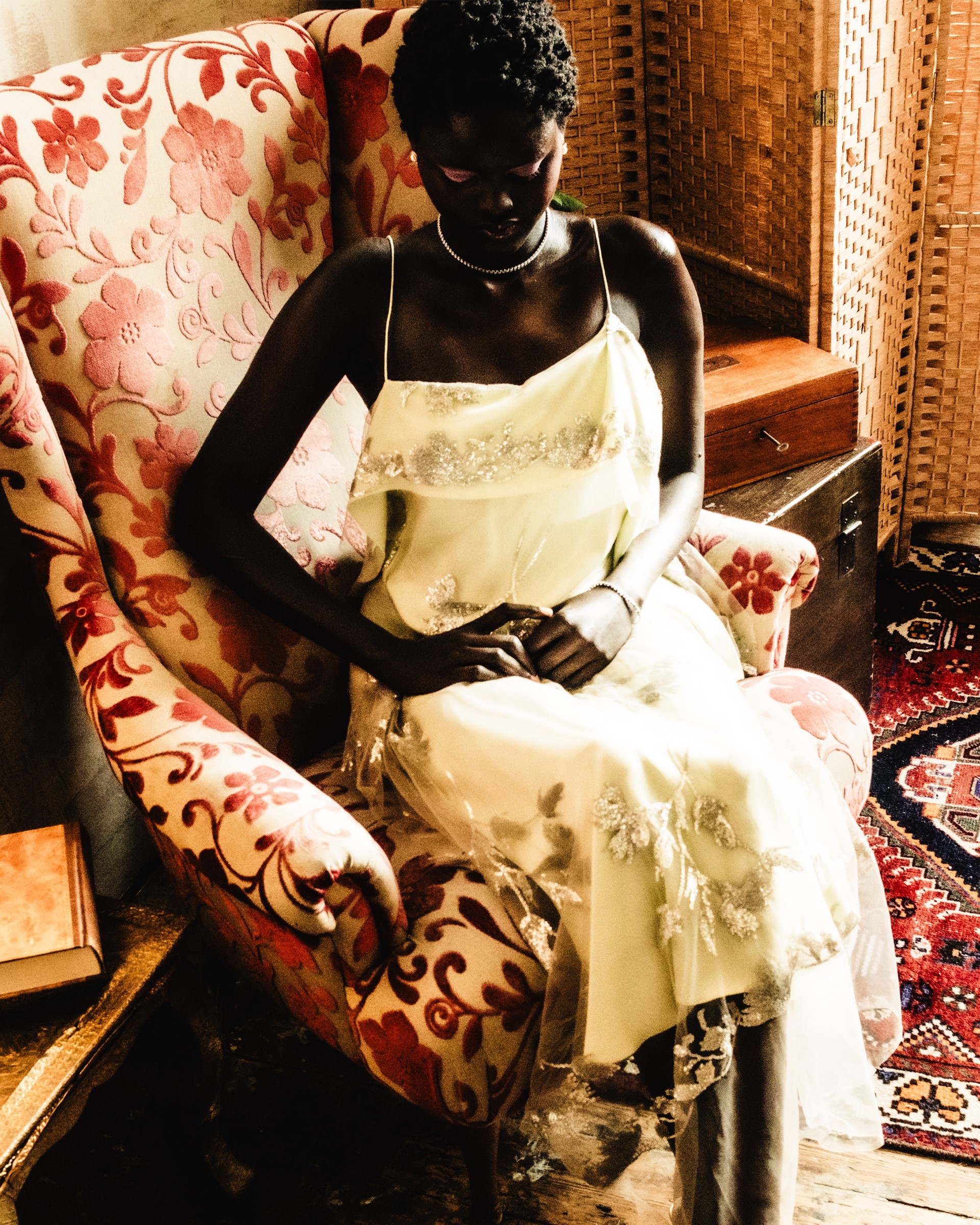 Elegant woman in vintage floral chair, wearing a shimmering dress, cozy ambiance.